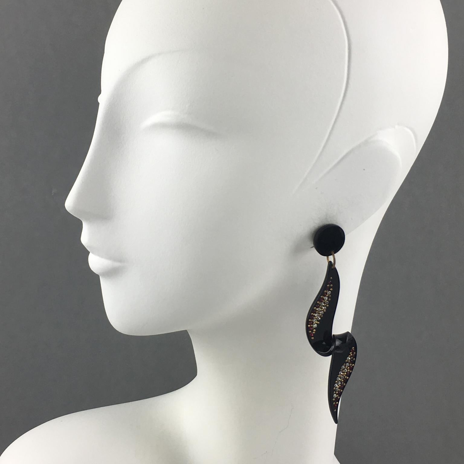 These spectacular long Lucite dangling clip-on earrings feature a geometric dimensional coiled pattern in shiny black color ornate with red and clear tiny crystal rhinestones and brass studs. They have the regular French clip back. There is no