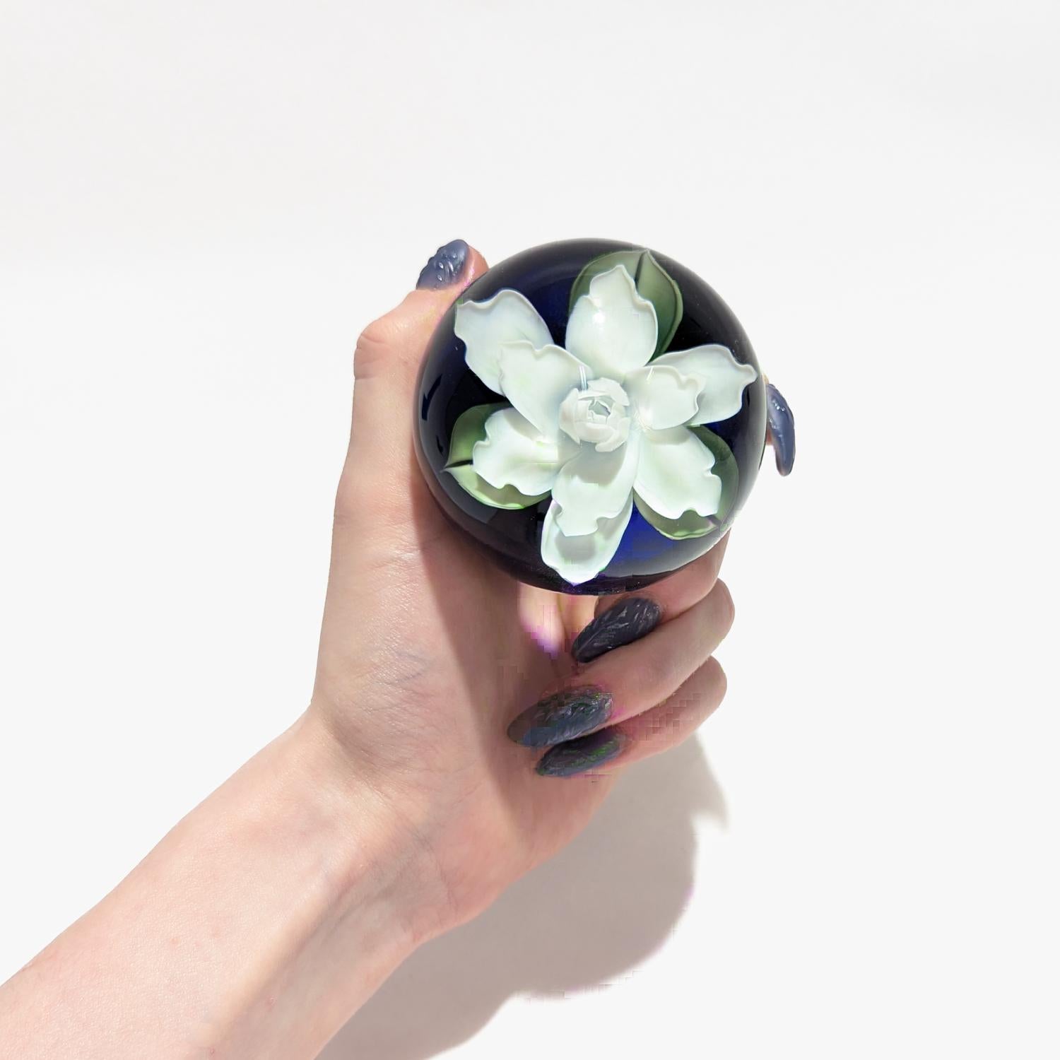 A fine Lundberg Studios paperweight by Daniel Salazar.

By Daniel Salazar for Lundberg Studios.

With a white lampwork gardenia with three green leaves on a cobalt blue ground.

With etched signatures to the base: Lundberg Studios / 1994 / 092810 /