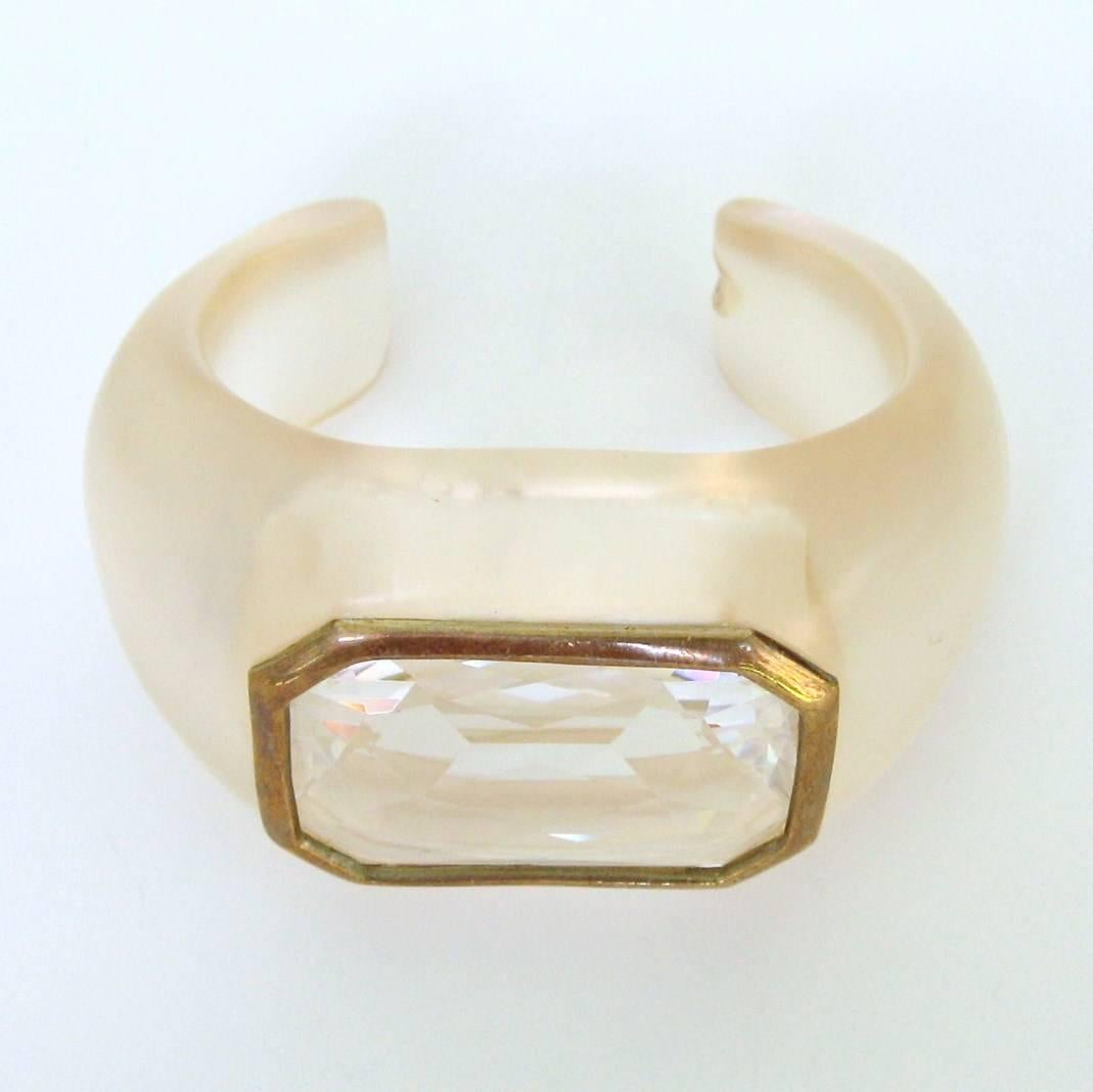 C'est un coup d'éclat. Un énorme cristal Swarovski serti dans un bracelet manchette en Lucite transparent. Lunette en cristal magnifiquement sertie au centre de la manchette. Le cristal est à facettes. Mesures : 43,6 mm de haut en bas La lunette