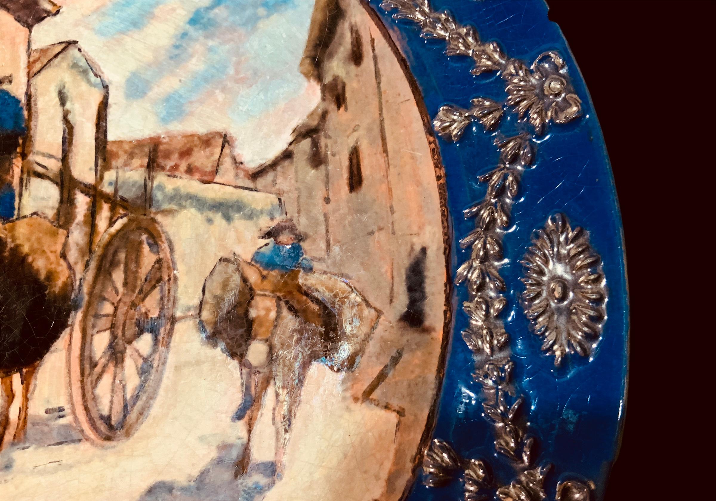 This is a Daniel Zuloaga Boneta (1852-1921) decorative hand painted wall plate. It depicts in the center a rural Spaniard village street scene of two peasants. One is riding his donkey that is carrying a double basket in its body and the other one