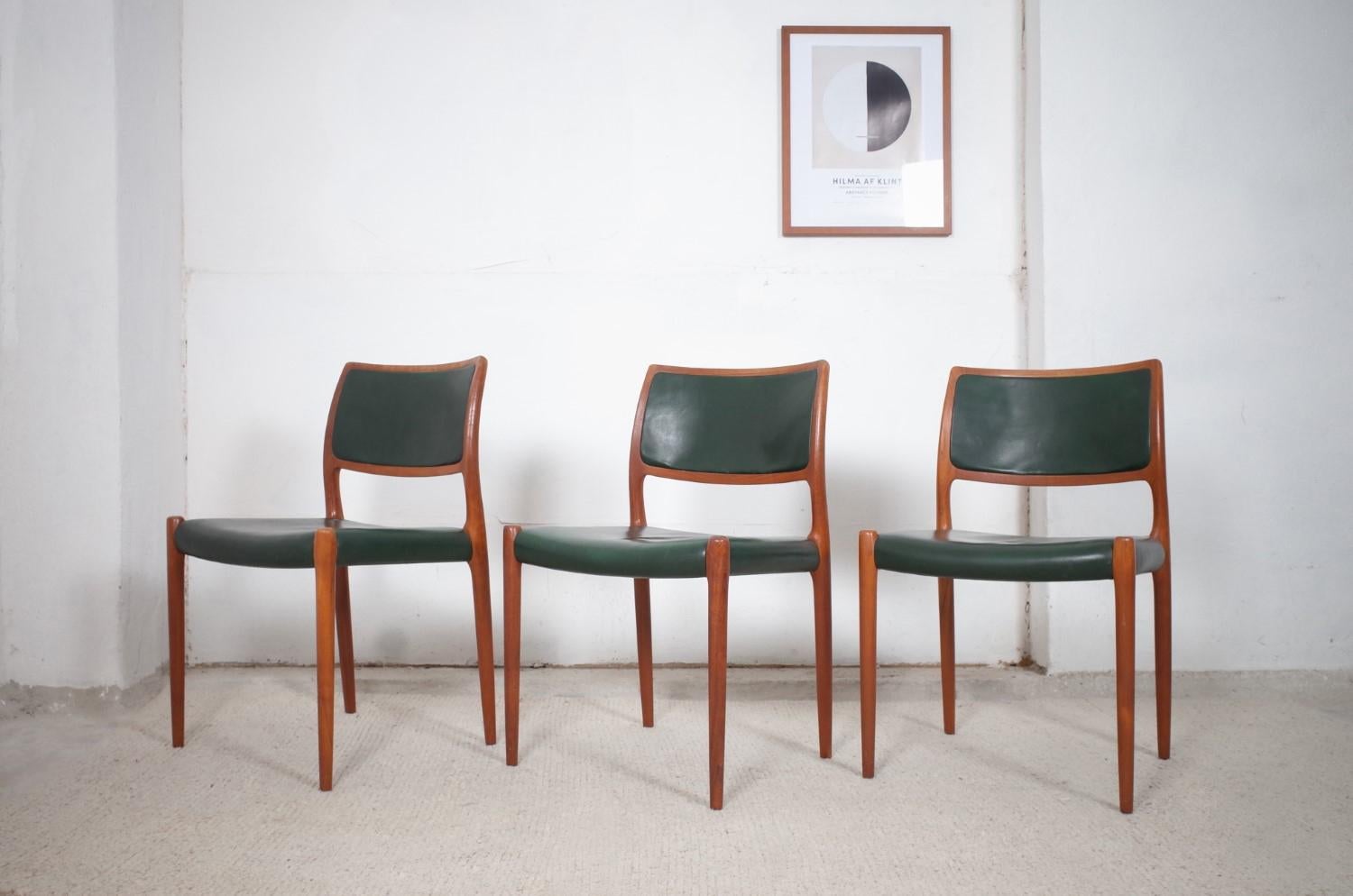 Zum Verkauf stehen drei klassisch schöne Teakholz Modell 80 Stühle von Niels Otto Moller für JL Møllers. Sie sind mit dunkelgrünem Leder bezogen, das sich perfekt in die Stuhlform einfügt. Die Stühle befinden sich in einem guten Originalzustand,