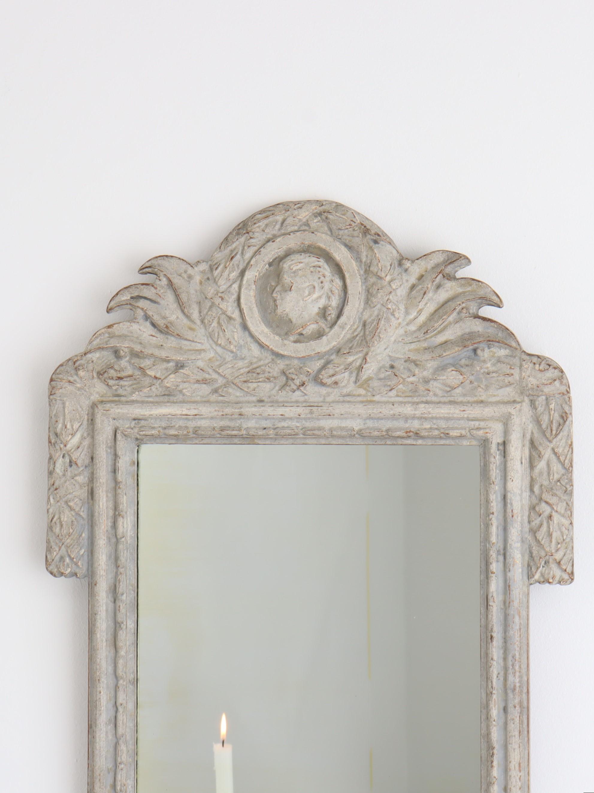 A Danish gray painted wood mirror from circa 1800 with carved crest. This exquisite Danish painted wood mirror, dating back to circa 1800, showcases the refined elegance characteristic of its era. The mirror is adorned with a beautifully carved