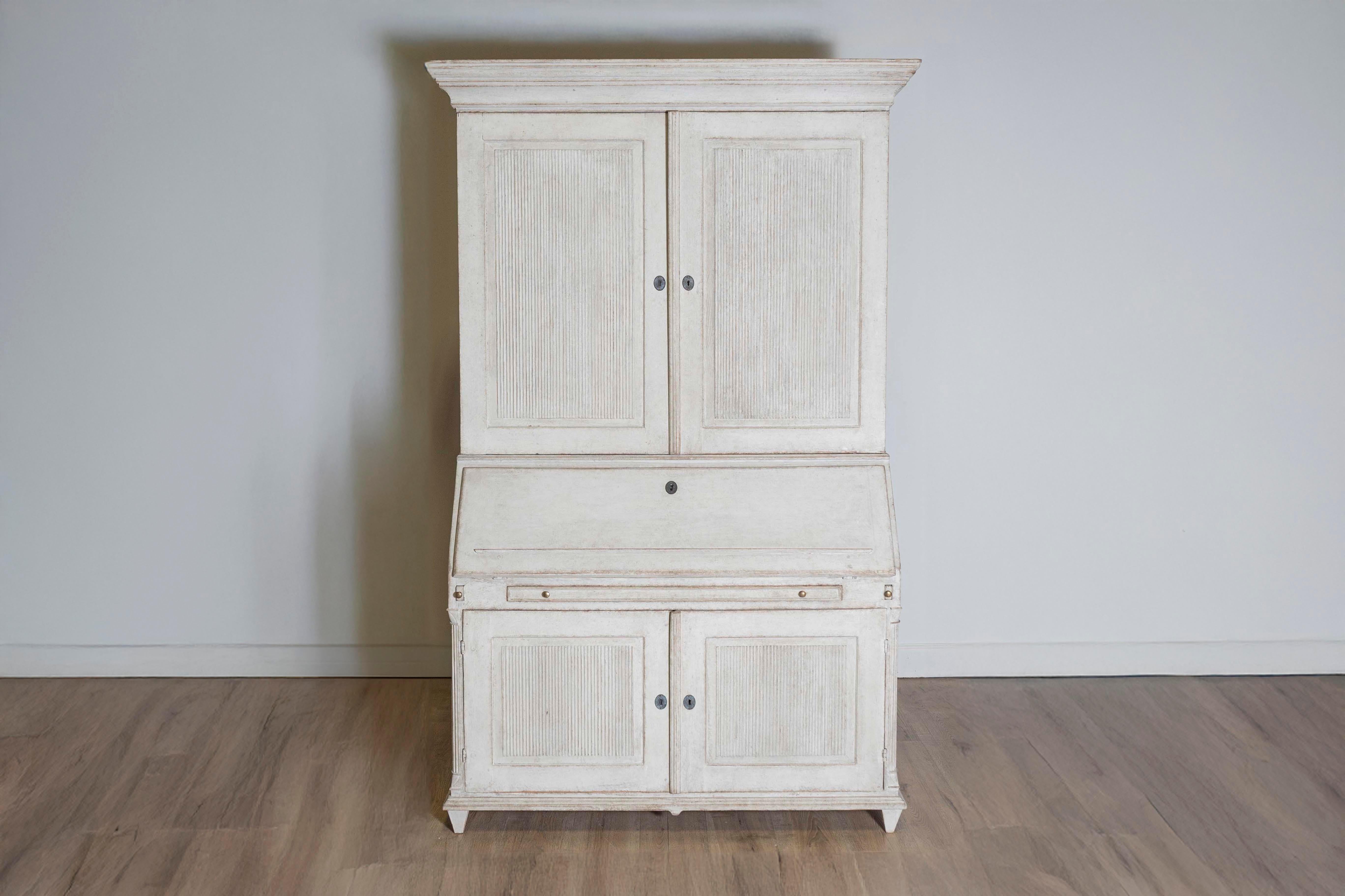 A Danish painted wood two-part secretary from circa 1810 with beige / light gray painted finish, slanted desk, four doors and carved reeded panels. A testament to timeless Danish craftsmanship, this two-part secretary from circa 1810 seamlessly