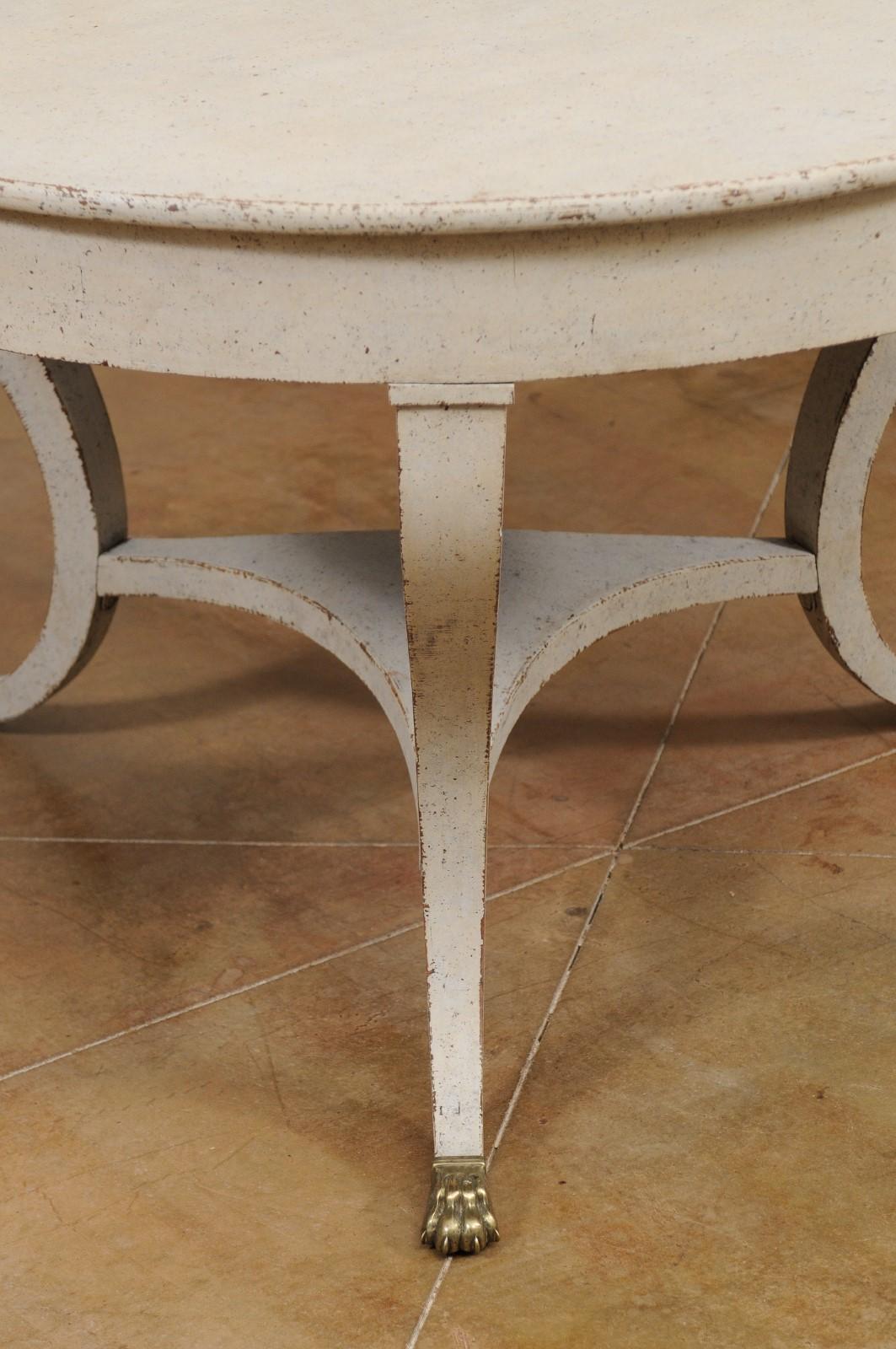 A Danish painted hall center table from the early 19th century, with curving legs and brass lion paw feet. Created in Denmark during the first decade of the 19th century, this center table features a circular top sitting above three curving legs