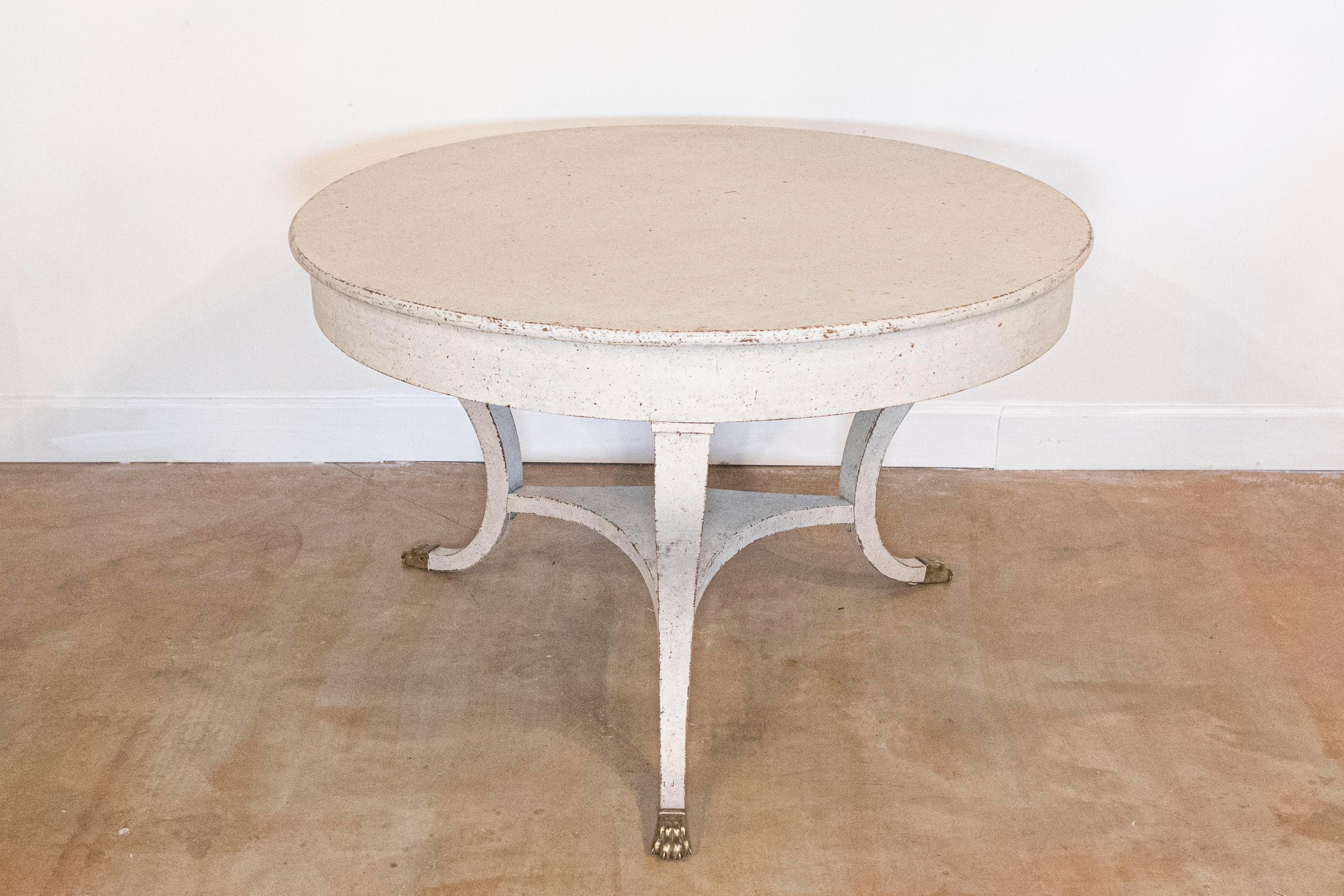 A Danish painted hall center table from the early 19th century, with curving legs and brass lion paw feet. Created in Denmark during the first decade of the 19th century, this center table features a circular top sitting above three curving legs