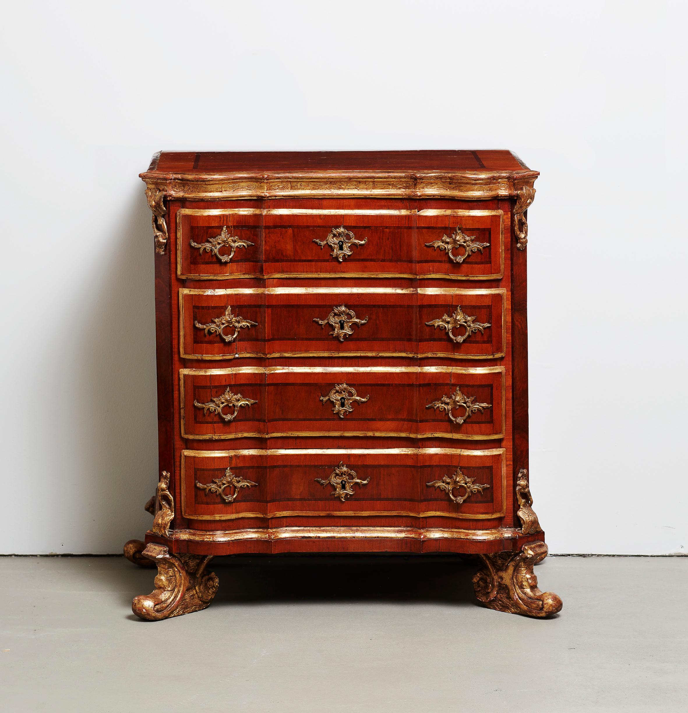 A very charming and small Danish parcel-gilt walnut and burr-walnut commode by Mathias Ortmann, mid-18th century. The shaped veneered top above moulded frieze with punched ground incised with foliate decoration above four shaped drawers flanked by