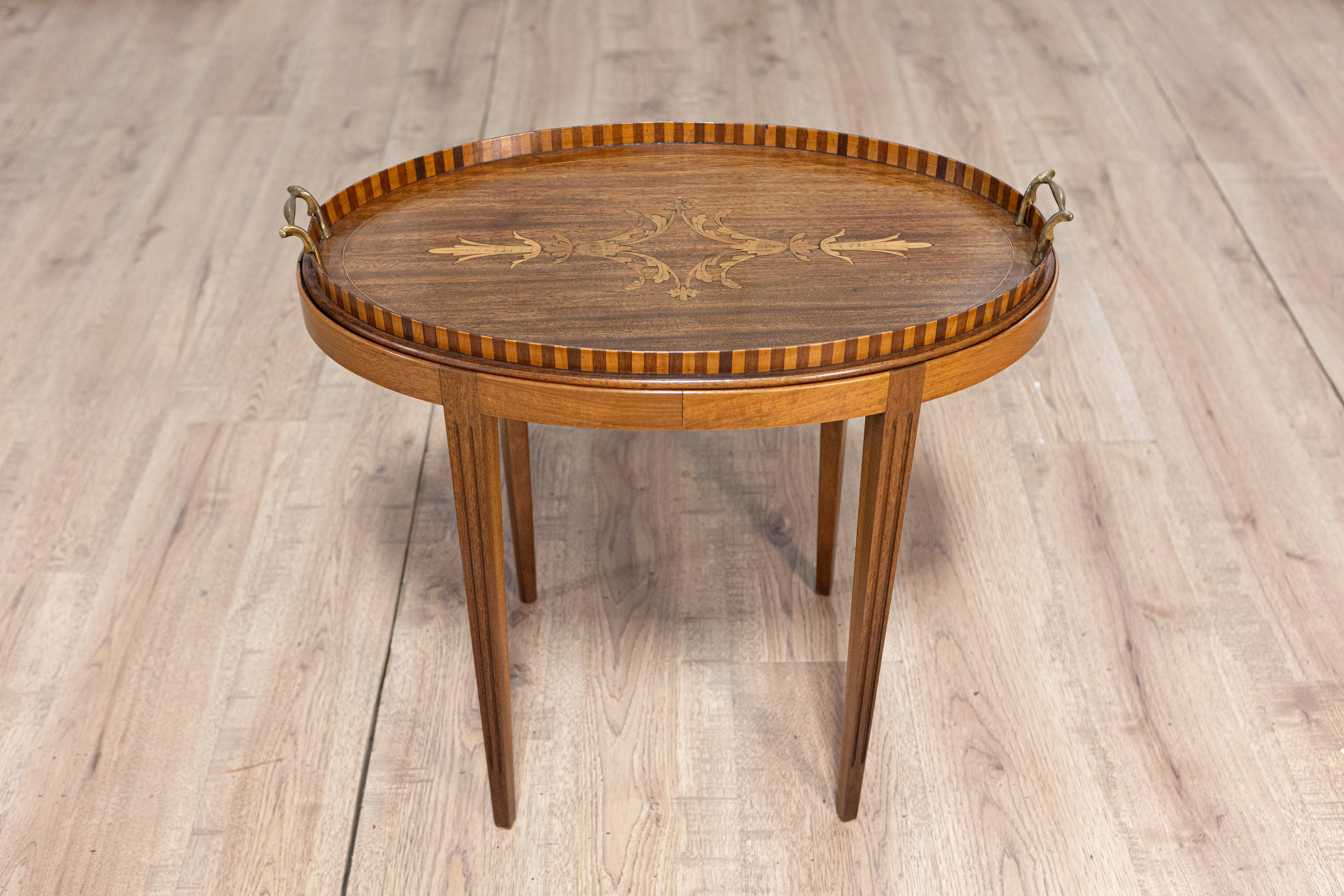 Tavolo danese in noce e frassino del 1900 circa con intarsi a fogliame e gambe affusolate. Questo tavolo danese in noce e frassino, risalente al 1900 circa, emana un'elegante miscela di praticità e artigianato artistico. Il piano ovale, un elemento