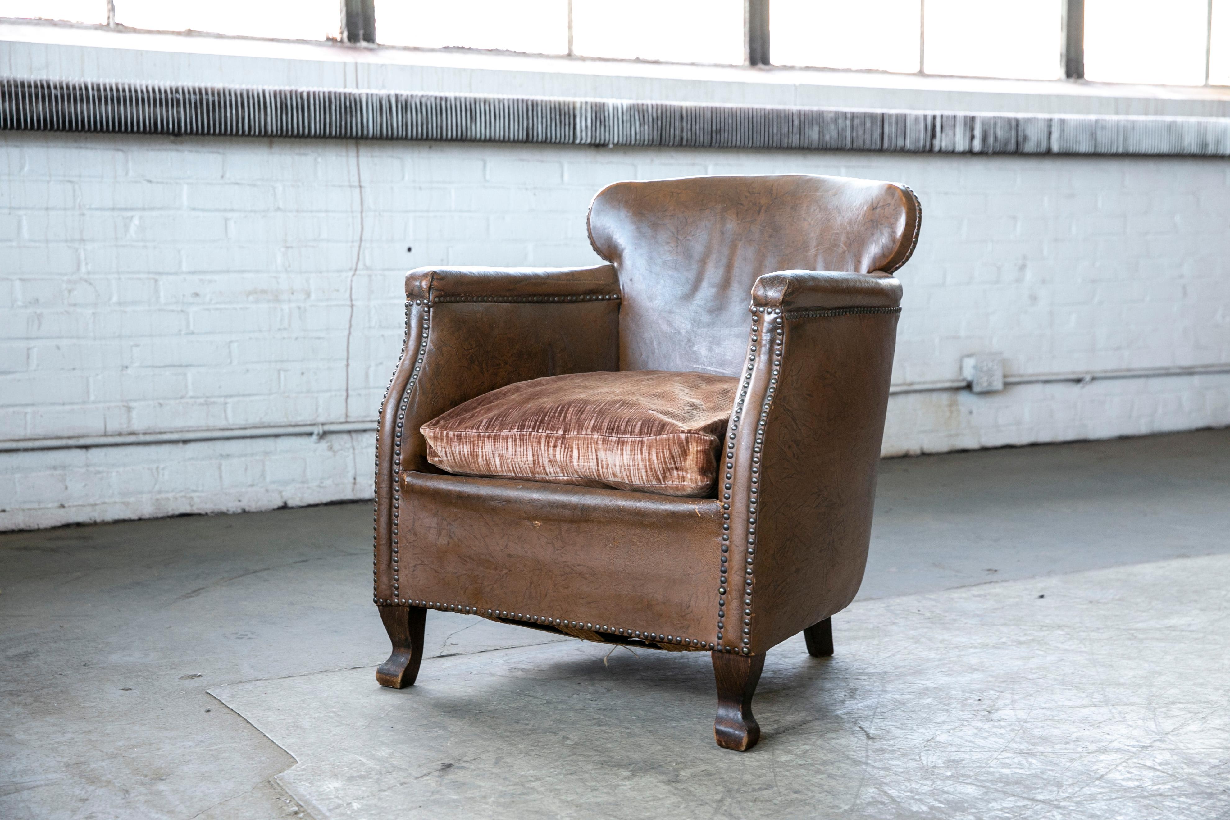 Charming small scale Danish club chair made by Danish Furniture Maker Oskar Hansen around the mid-1930s. Covered in original cognac brown leather with a smooth back and brass tacks in the armrests. Coil springs in the seat. Overall good condition