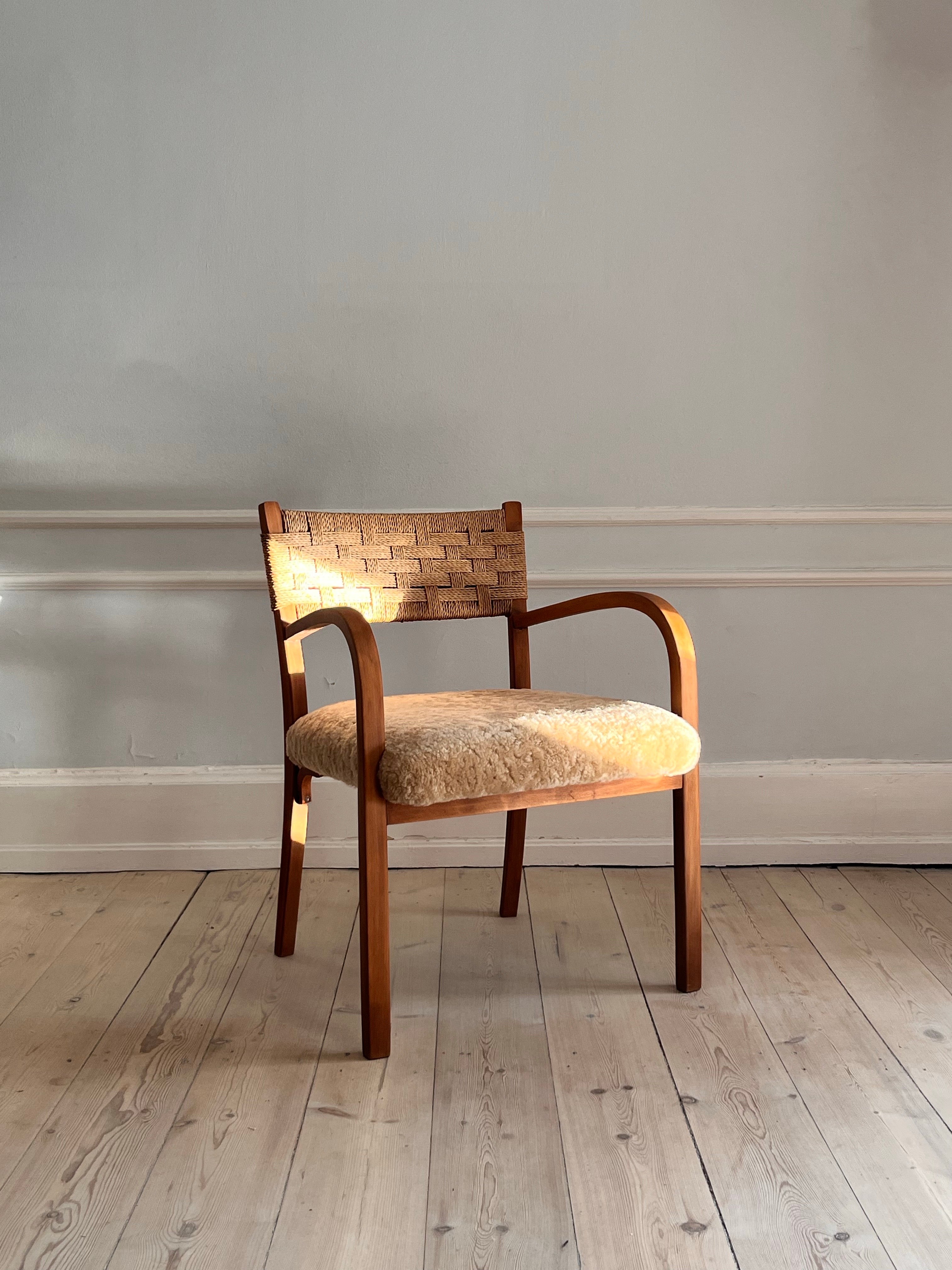 Armchair from approx. 1930s in beech wood and wicker in the back.

The seat of the chair is reupholstered by a professional seamstress in soft, honey-coloured lambskin. 

Unique with its curved armrests and the combination of wicker, wood and