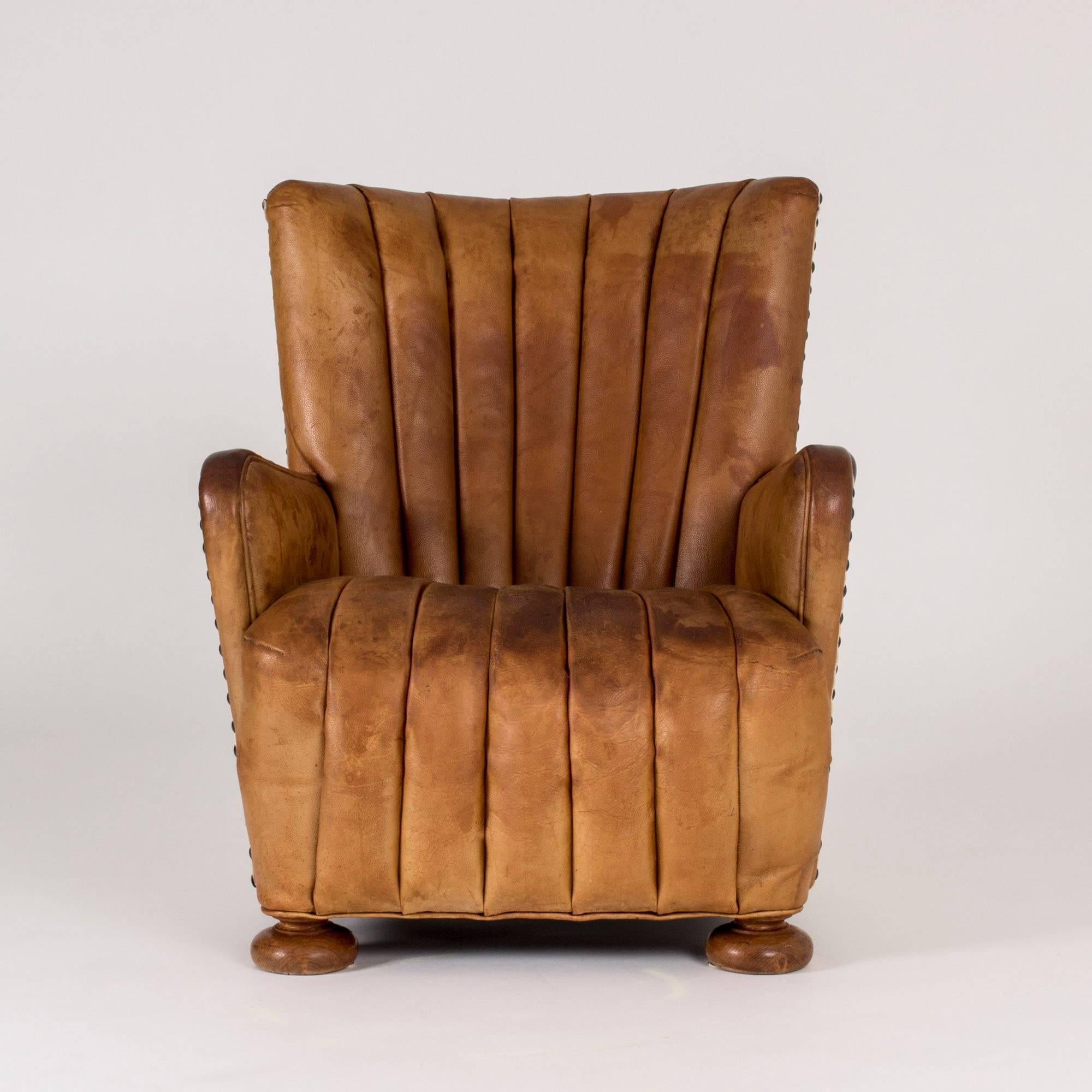 Imposing Danish 1930s lounge chair with just the right amount of slouch. Upholstered with leather in the front and with cream-colored linen in the back, adorned along the edges with brass decorative nails. High quality leather in good condition and
