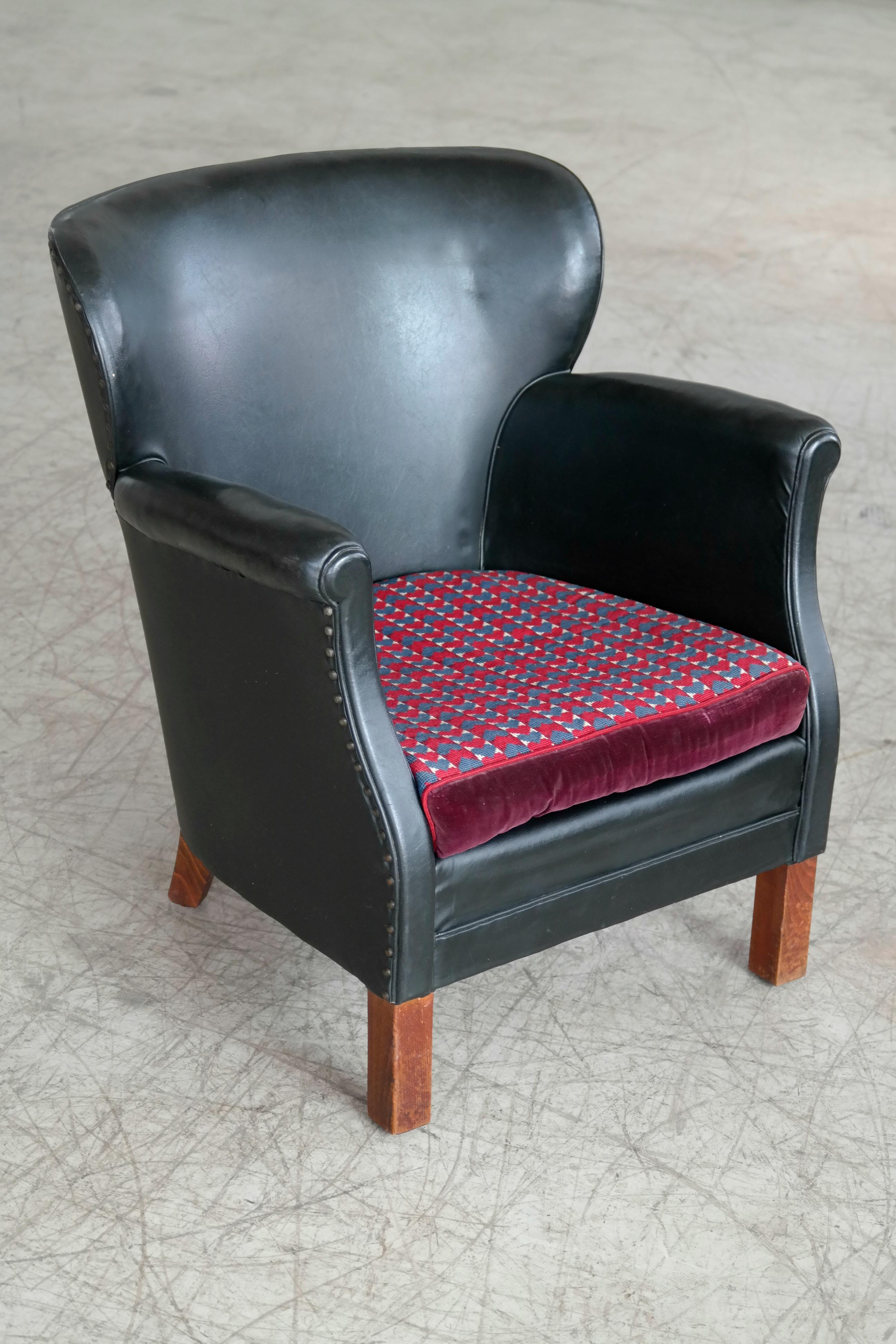 A Classic Danish small scale club chair from the post Art Deco period of the late 1930s. Fantastic patinated original black leather with a smooth back and brass tacks. Later added cushion. Noble patina and wear to especially the armrests. Fantastic