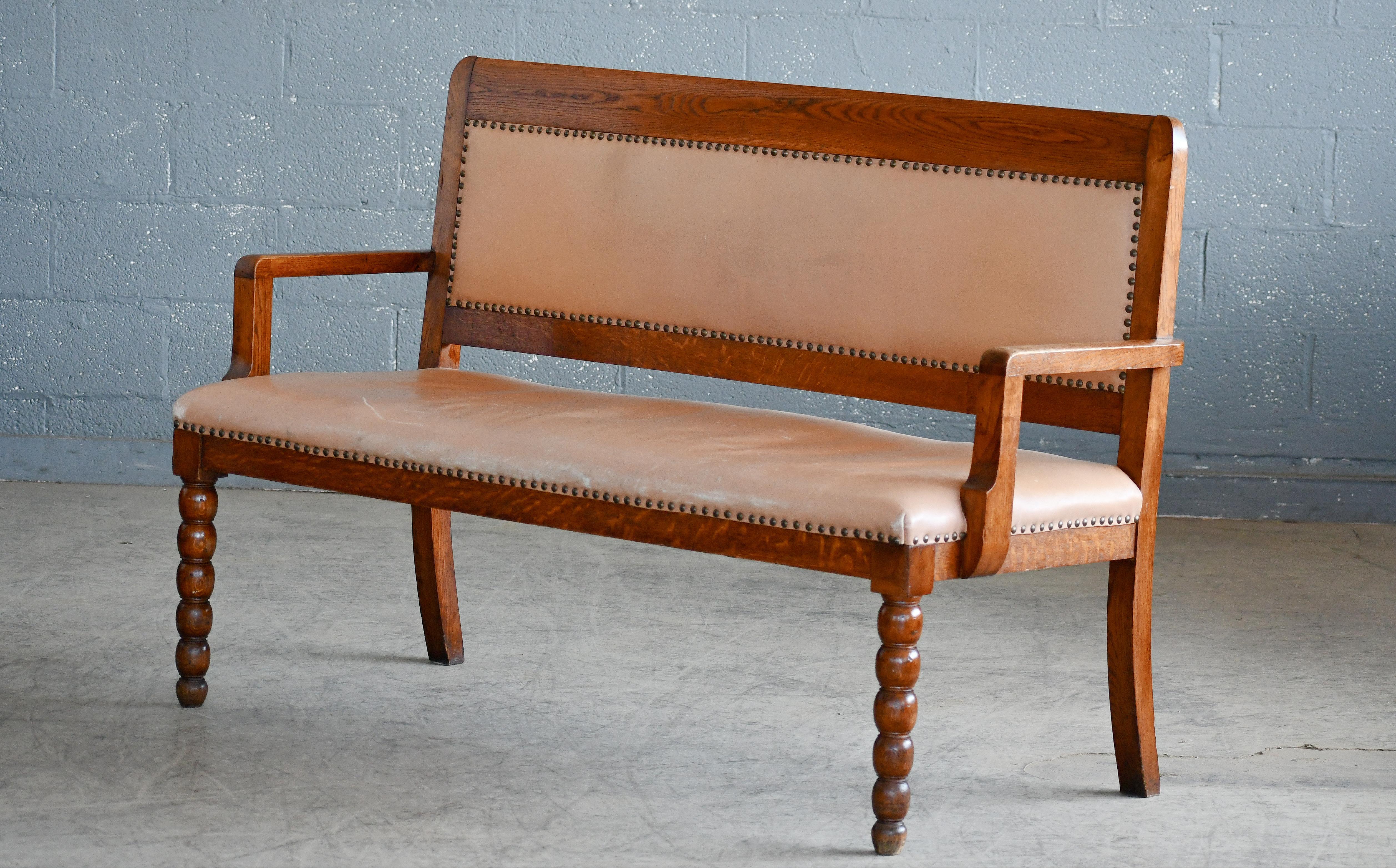 Rare bench from the nearly mid-century - probably made in the 1920 from carved oak and later reupholstered in a tan leather. Simple yet very refined design with beautiful wood grain and patina. Leather showing some wear and patina but is in very