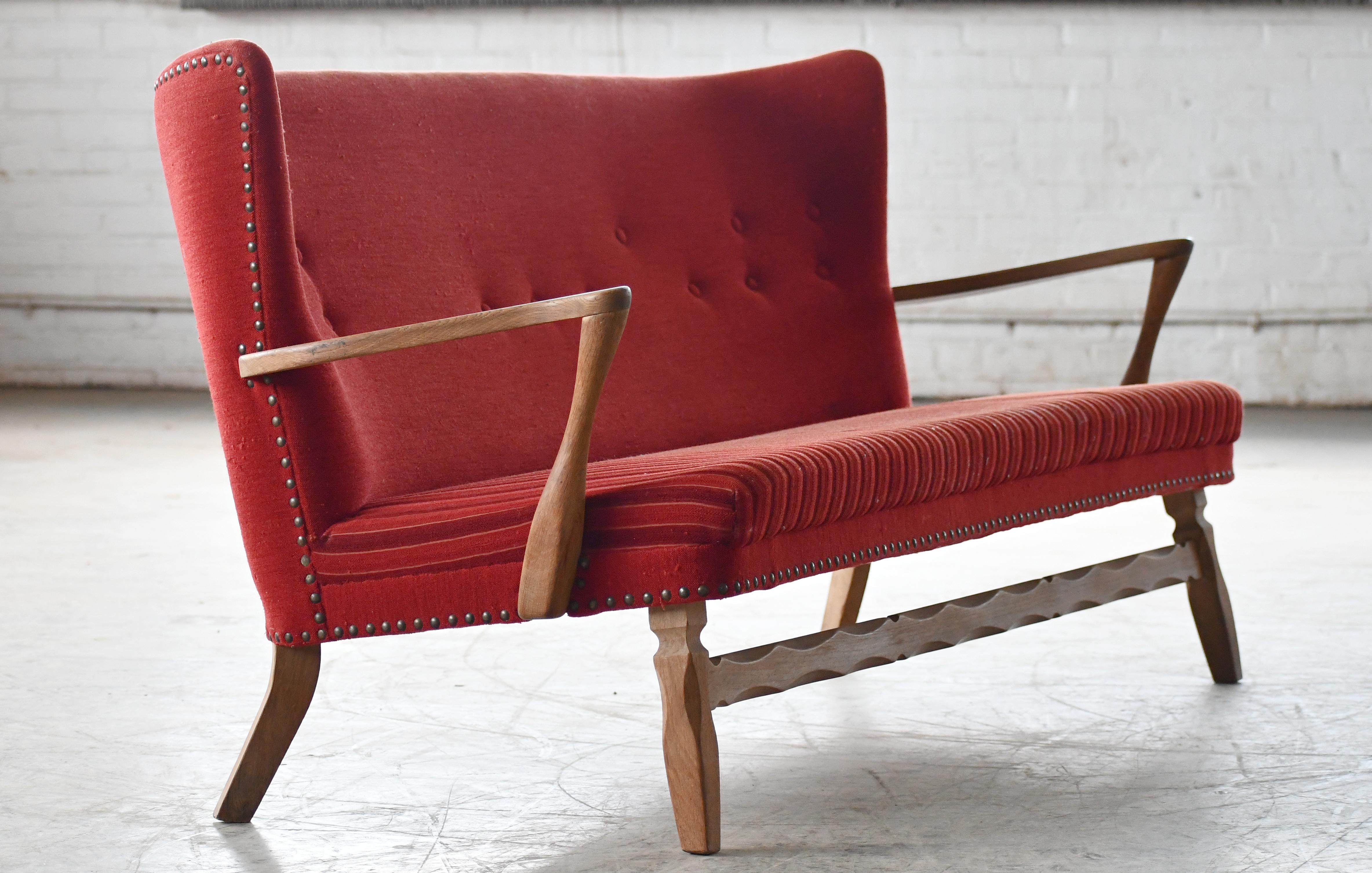 Fantastic 1950s Settee in red wool and beautifully carved oak base and open armrests. Very refined clean lines and an almost benchlike style to the settee. It's an unusual piece and hard to date but most likely made in the 1950s. Wool fabric is