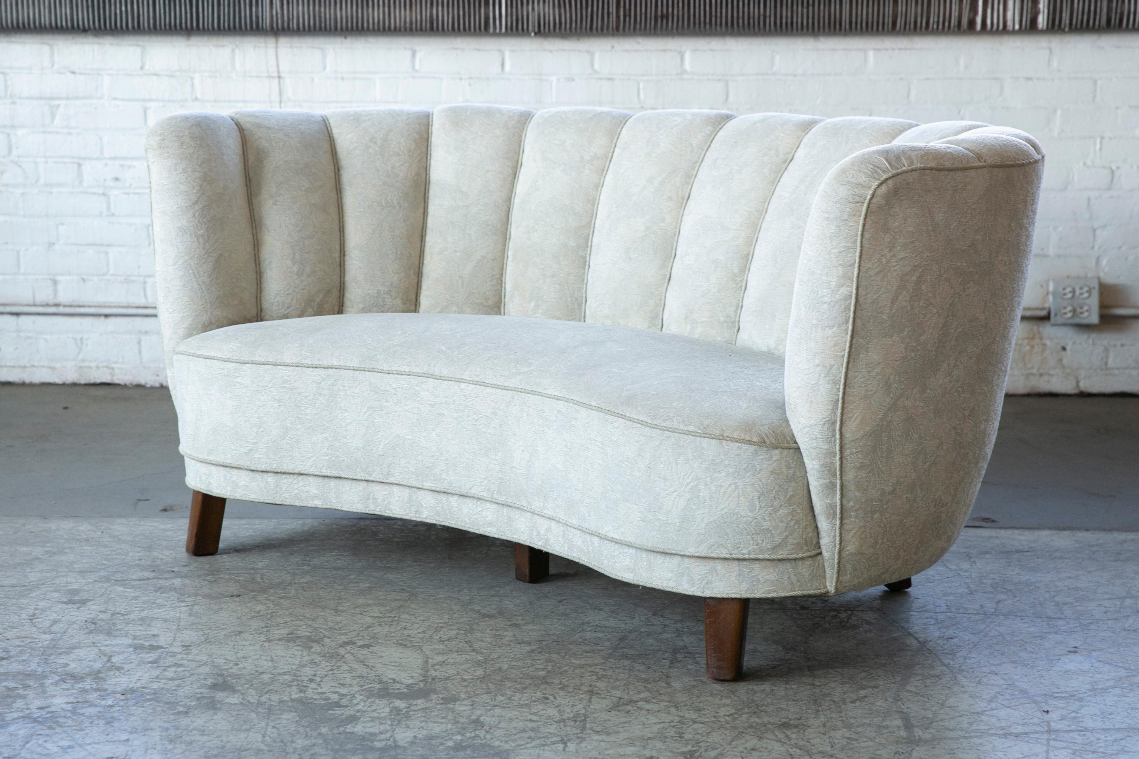 Viggo Boesen style banana shaped or curved Loveseat made in Denmark, circa 1940. This small sofa will make a strong statement in any room. Beautiful round voluptuous lines and with large block legs. Re-upholstered at a later point in a whitish