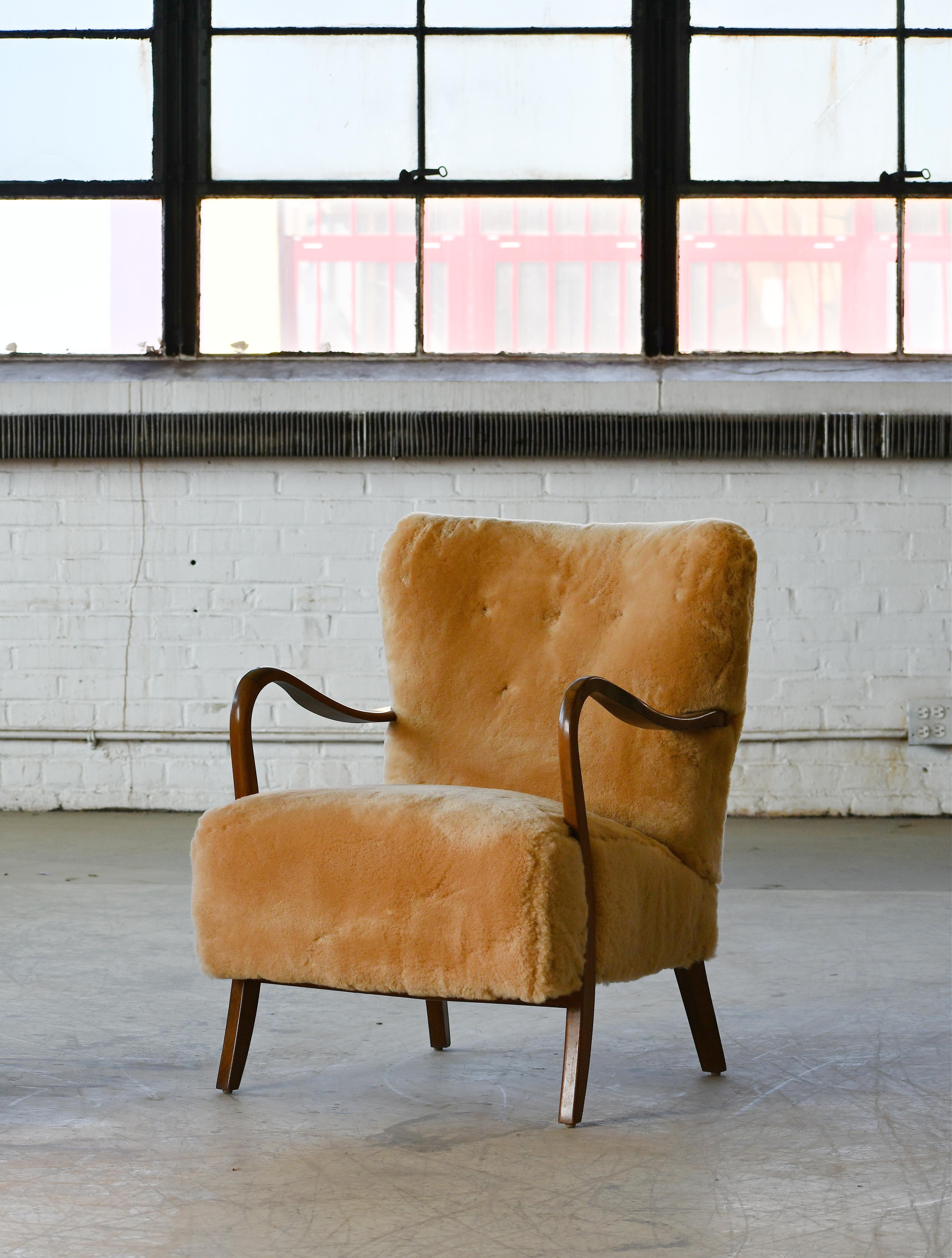 Classic elegant Danish low back armchair from the 1940s by Alfred Christensen for Slagelse Mobelvaerk with open armrests in beautifully curved stained beech. We have reupholstered the chair in exuberant amber colored straight fleece sheepskin by