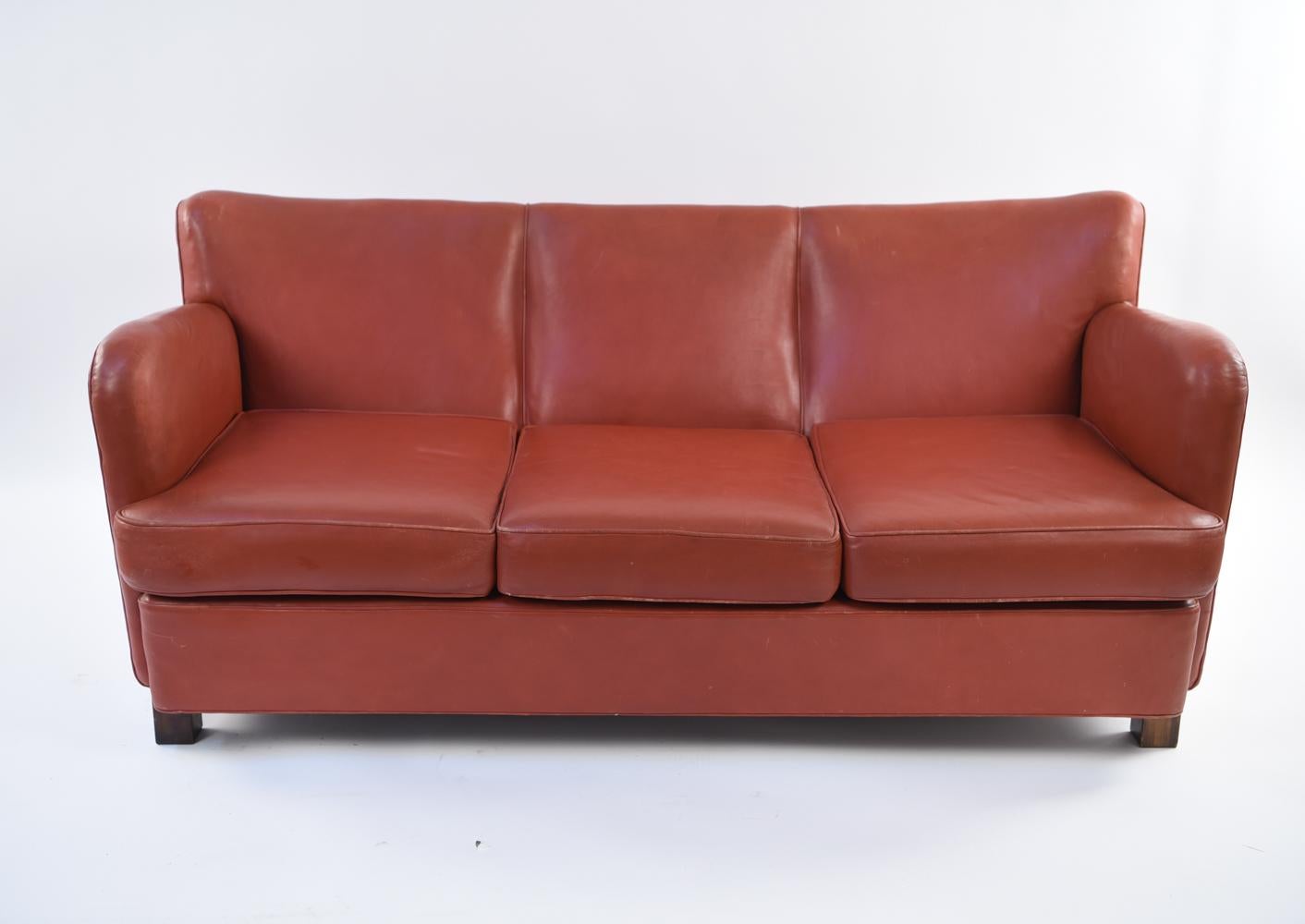 This Danish sofa is a statement piece in the manner of Mogens Lassen with elements of Art Deco style. Upholstered in a tasteful red, this sofa has a bold but sophisticated feel with clean modern lines. A great clean slate to be upholstered to your