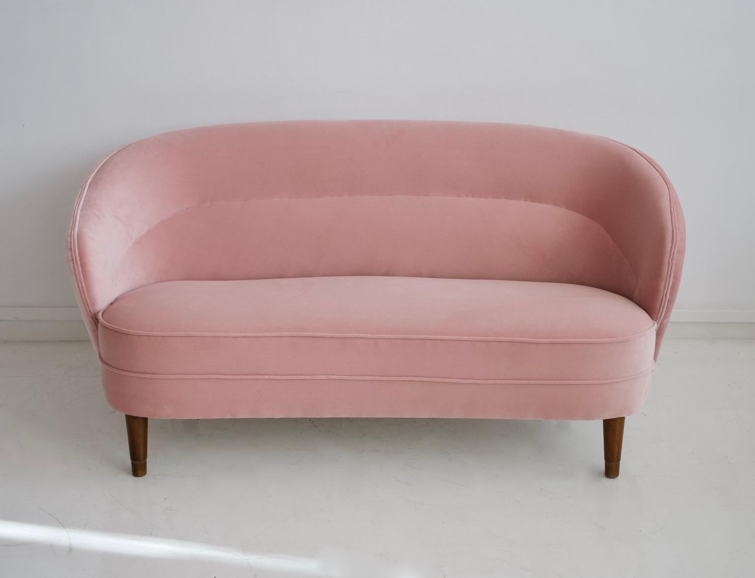 Slightly curved sofa with legs of stained beech from circa 1940s. Made by a Danish furniture producer. Reupholstered in light pink velvet.