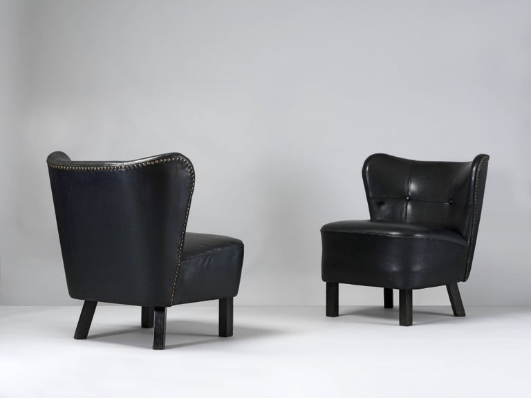 A pair of 1940s modernist lounge chairs. An early example of traditional Danish cabinet making with original black dyed leather upholstery and brass nails framing the back and wooden legs with original matte black paint.

Produced in an era