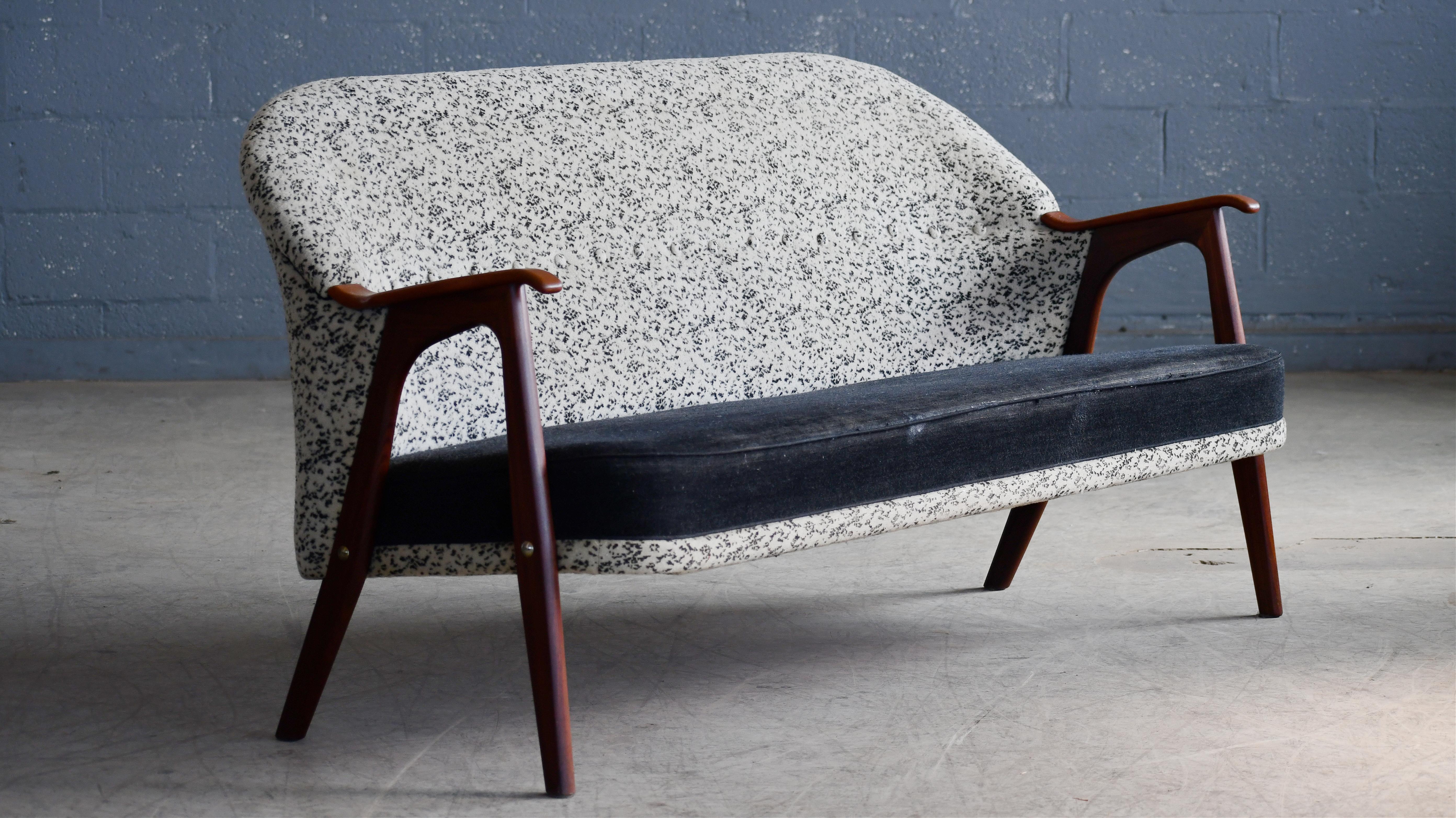 Affascinante poltrona danese degli anni '50 con gambe e braccioli in teak. Il design ricorda molto lo stile di Arne Hovmand-Olsen e ha un design versatile. Il divano è ancora rivestito con il suo tessuto bicolore originale, ma presenta segni di