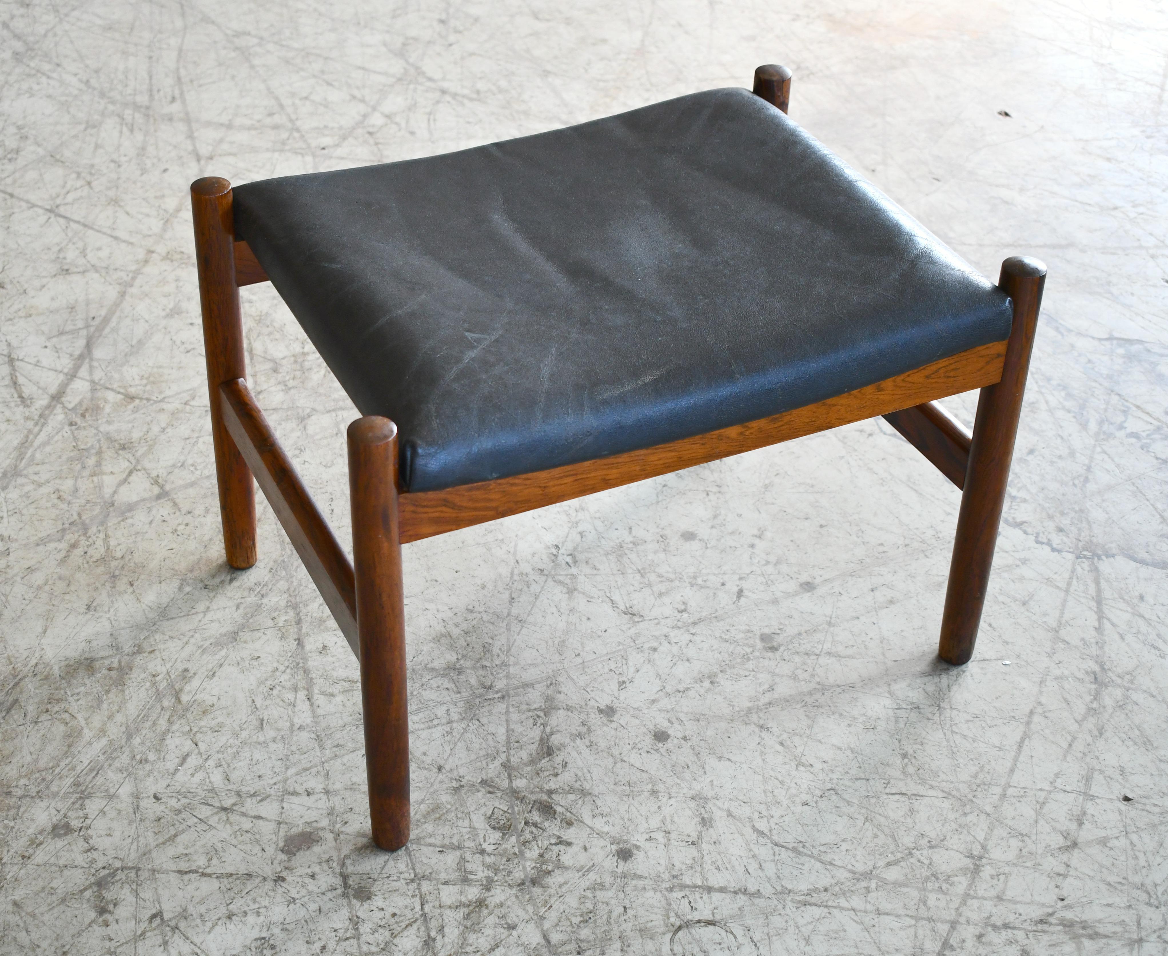 Spottrup's Classic and sought after ottoman featuring a solid rosewood frame with its original leather cushion in black well worn patinated leather. A great Danish midcentury design that could be paired with a chair as an ottoman or used alone as a