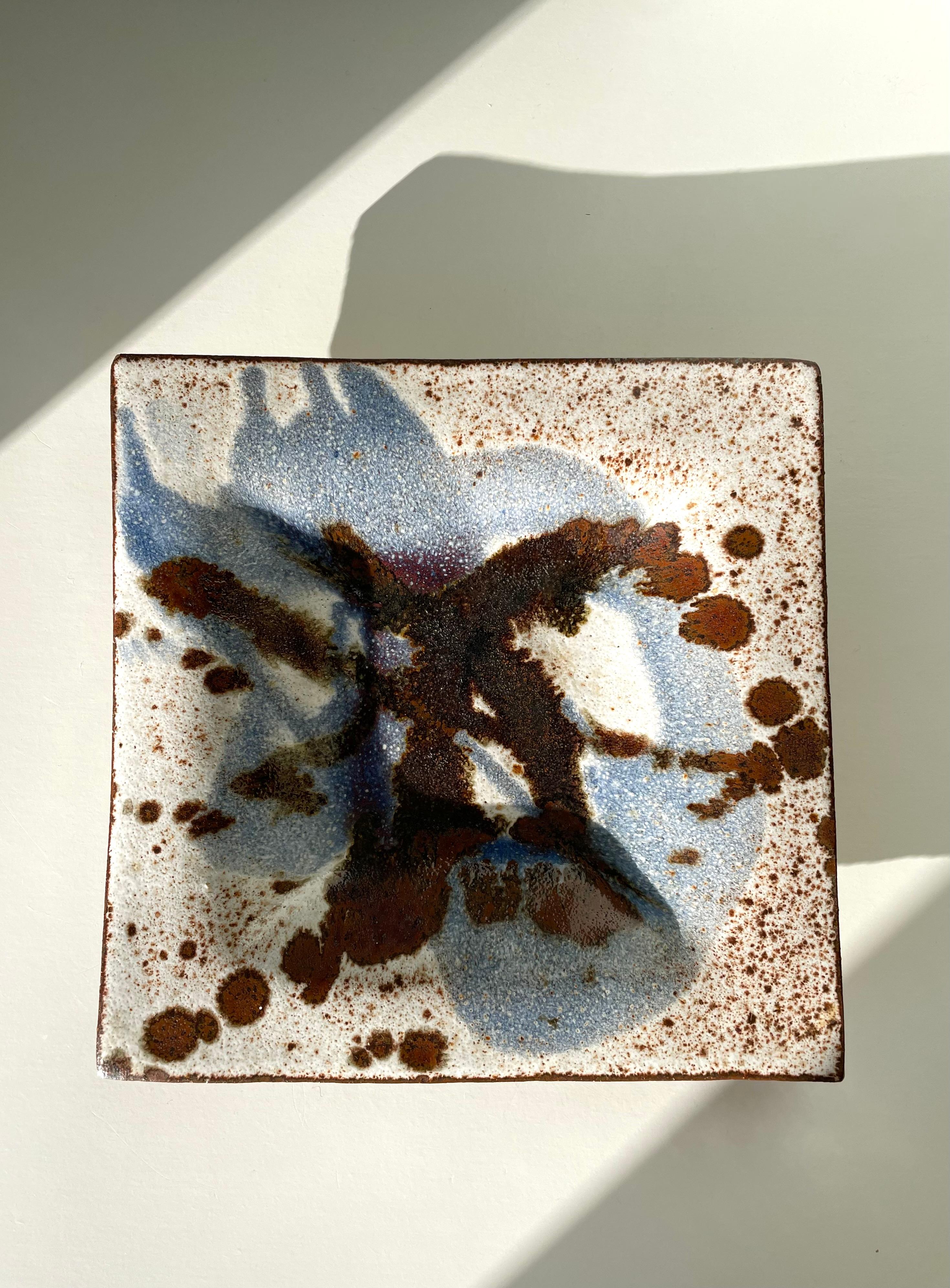 Ceramic wall plaque handmade by Danish artist Jørgen Finn Petersen in the 1960s. Square bowl shape making the item usable as a decorative dish or centerpiece as well as an art piece hung on the wall. Hand-painted spotted glaze in warm browns, light