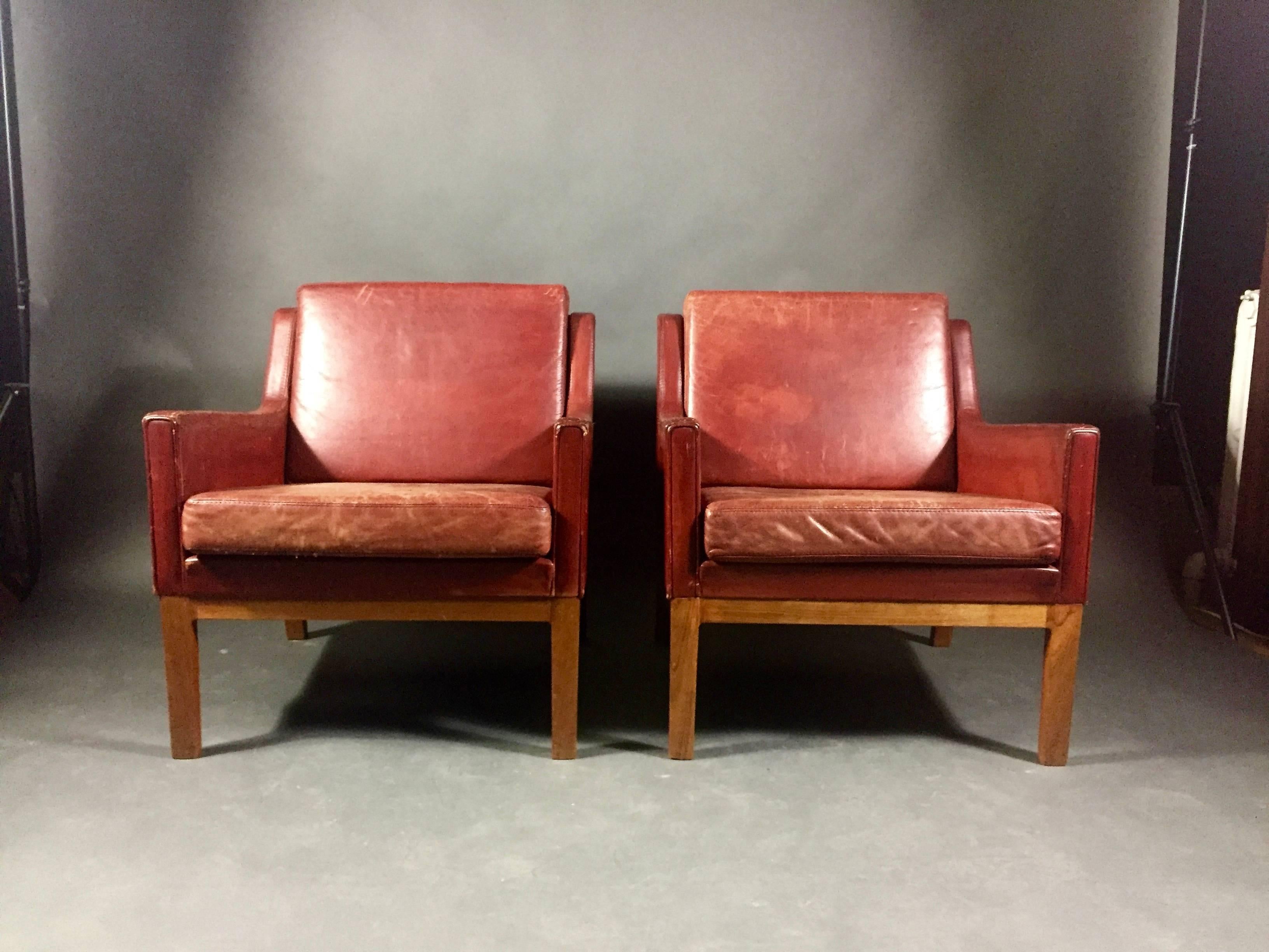 This is solid pair of Scandinavian red leather armchairs from 1960s, likely Danish with angled armrest over beech frame. Leather in good condition though overall scratches and later overdying evident in color - has beautiful vintage leather view.