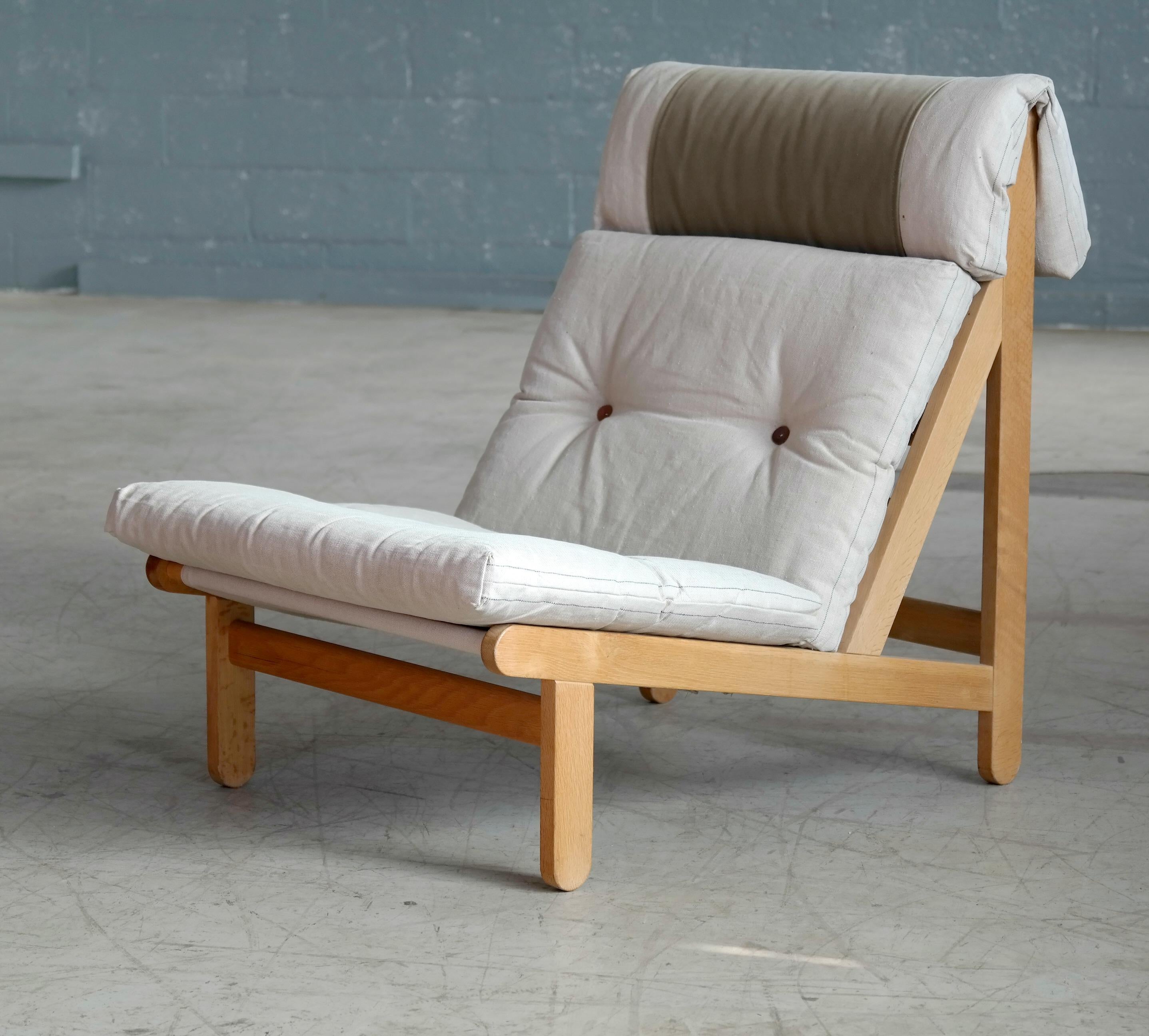 Rare and very sought after easy lounge chair designed by Bernt Petersen for Schiang Furniture of Denmark in 1966. Oak frame with loose cushions in seat and back upholstered with an off-white colored heavy canvas fitted with leather buttons. Neck