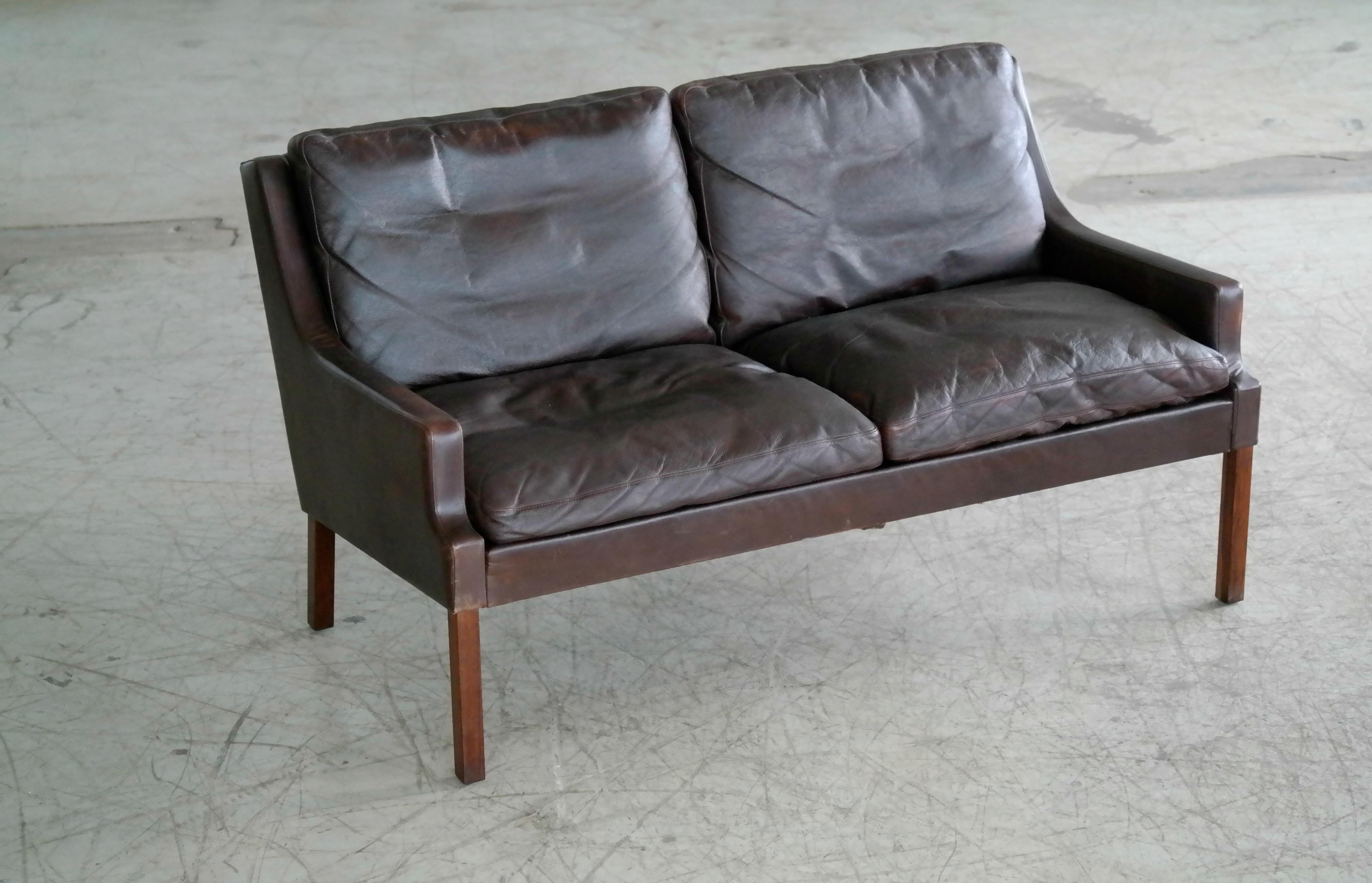 Classic Danish midcentury sofa by Georg Thams from the late 1960s. Slim beautiful silhouette similar to Hans Olsen's iconic designs raised on tall rosewood legs and with down filled cushions wrapped in espresso colored leather. Great patina and wear