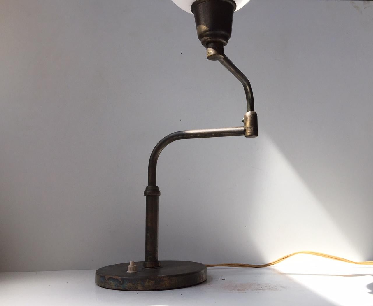 This table lamp is made of patinated solid brass with a spheric opaline glass shade. The piece features a swing arm mechanism as well as an on/off switch on the base. It was manufactured by Fog & Mørup during the 1930s. The style borderlines between