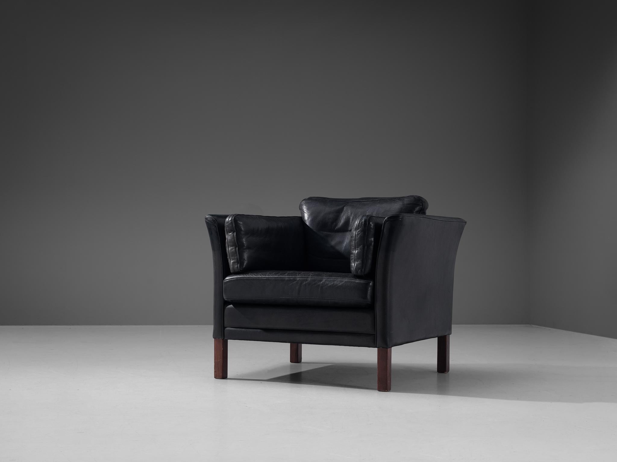 Armchair, leather, stained wood, Denmark, 1960s. 

This elegant armchair hails from Denmark, crafted in the 1960s. Upholstered in supple black leather and accented with stained wood, its design boasts distinctive outward-curving armrests, lending