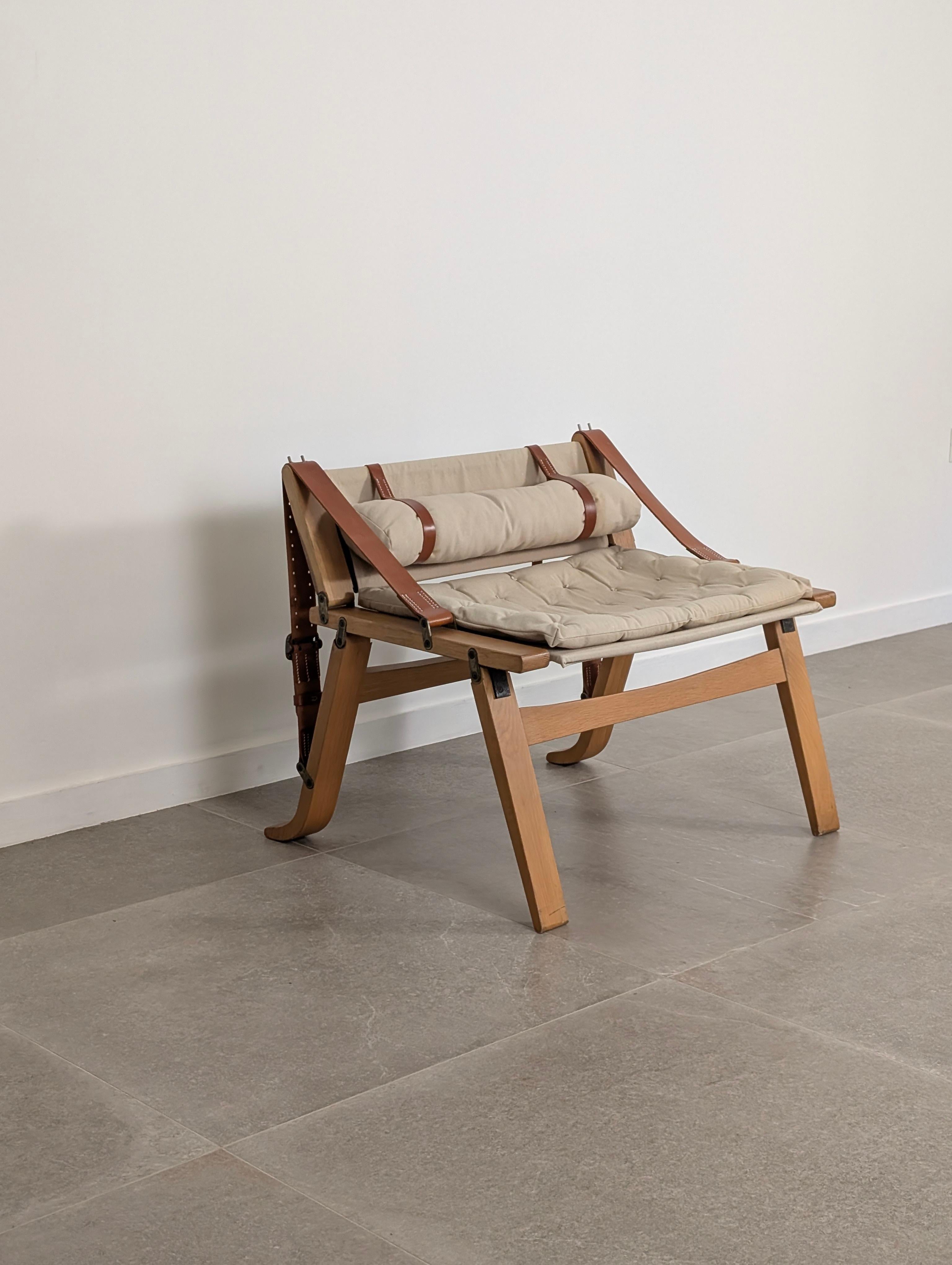 This Danish-designed armchair from the 20th Century features a distinctive style. Its structure is made of wood. The design is defined by its characteristic system of brown leather straps, which support the upholstery and contribute to its visual