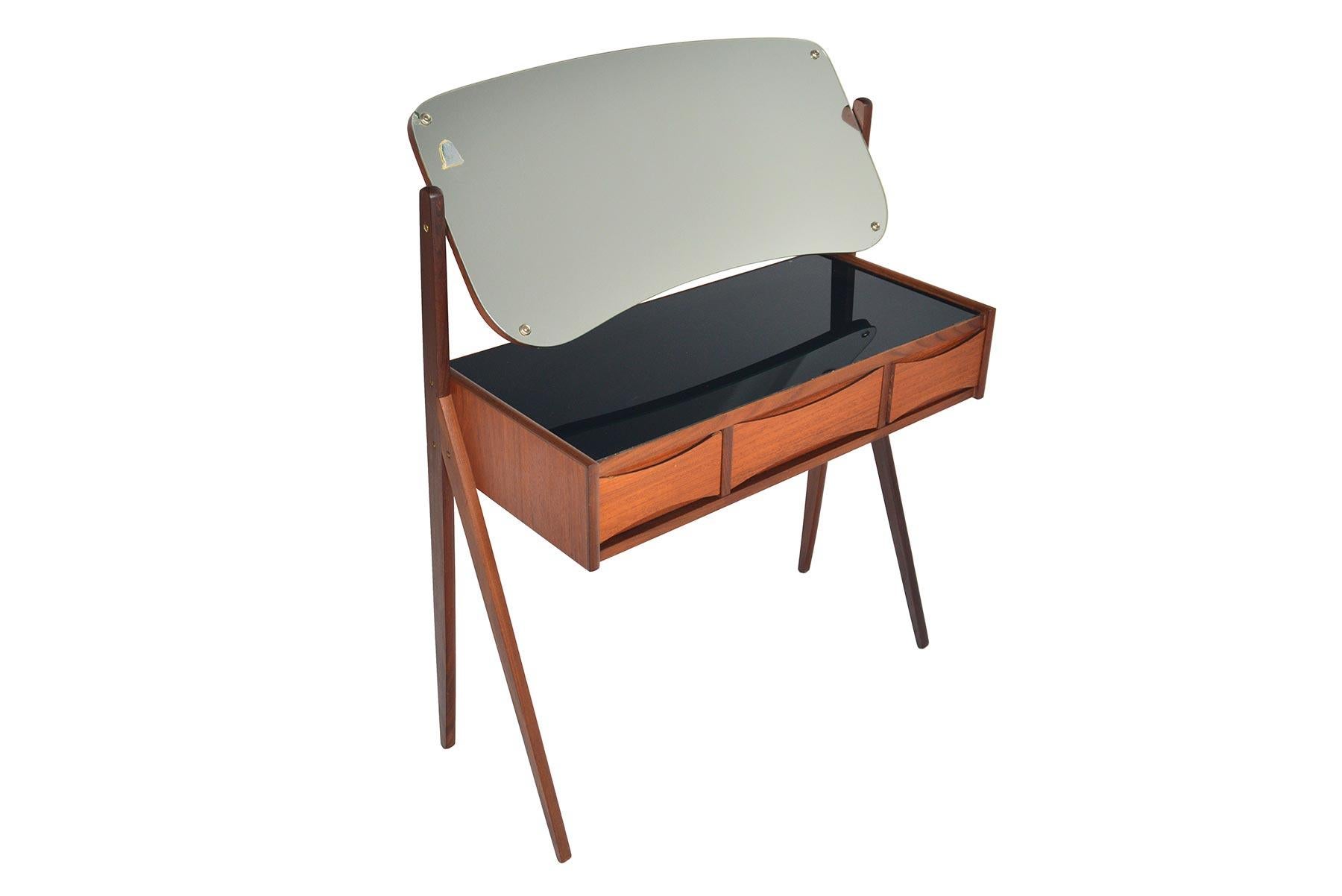 This gorgeous Danish modern Arne Vodder teak V-legged vanity offers wonderful lines in a small footprint! Featuring an articulating vanity mirror, this piece has ample storage with three drawers and a black glass, lined top. In excellent original