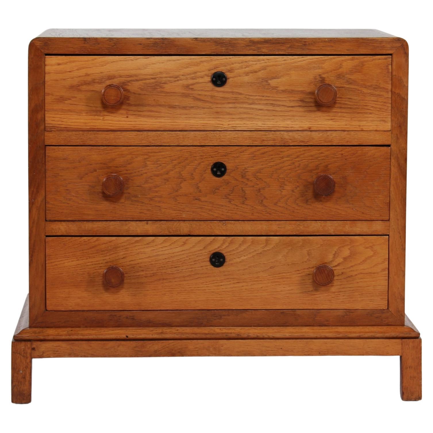 Danish Art Deco dresser with 3 drawers made of solid and veneered oak. The drawer knobs are hand-turned and the central keyhole fittings are made of black bakelite.

The chest of drawers is really cozy with round corners and fits well with modern