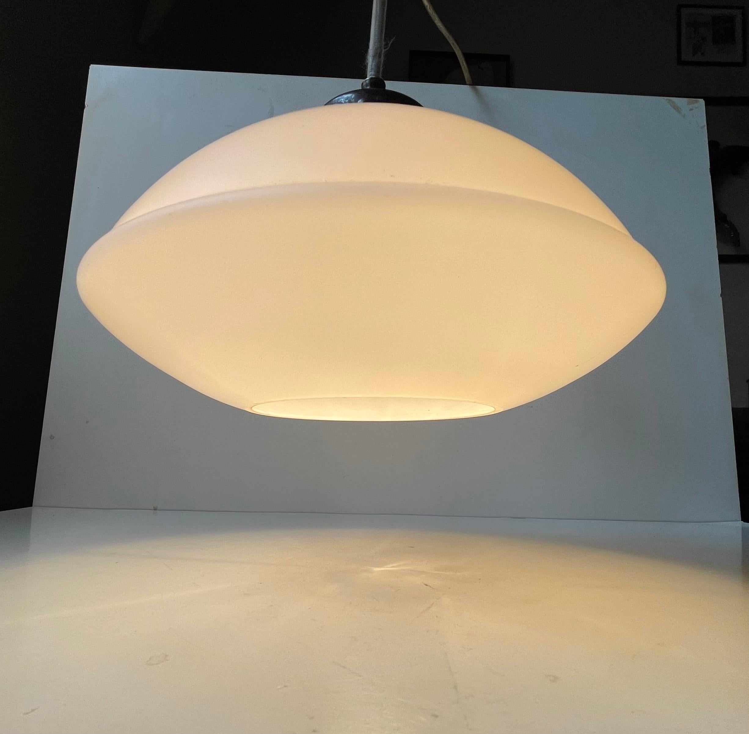 A stylish 1930s Bauhaus style, Funtionalist or Art Deco pendant lamp. It features a silver/nickel plated brass top, a ufo shaped matté opaline glass shade and its original porcelain bulb suitable for a lightsource/bulb up to 70 watts. Made in
