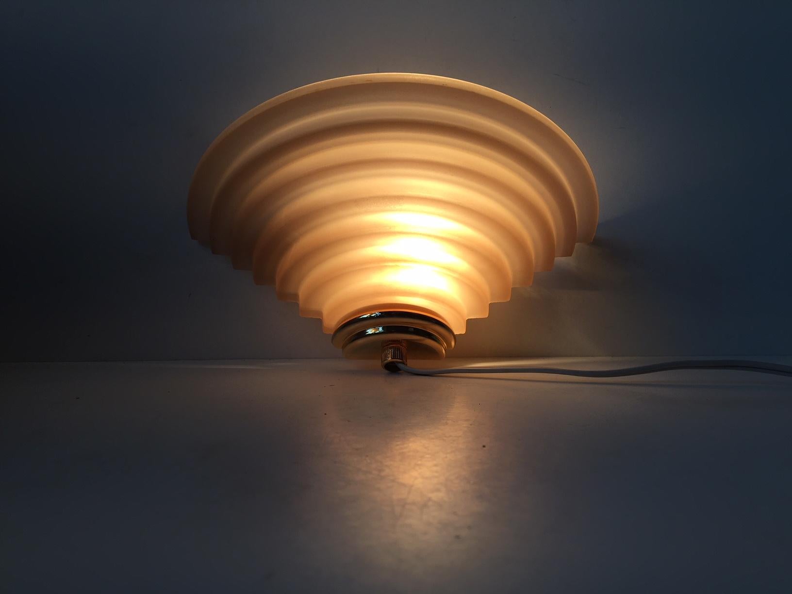 This up-light sconce was manufactured by EL-Light in Denmark during the 1970s. It is reminiscent of the architectural, skyscraper inspired approach of the 1920s. It is composed of light pink colored matte glass and has a gold-chromed end-piece.