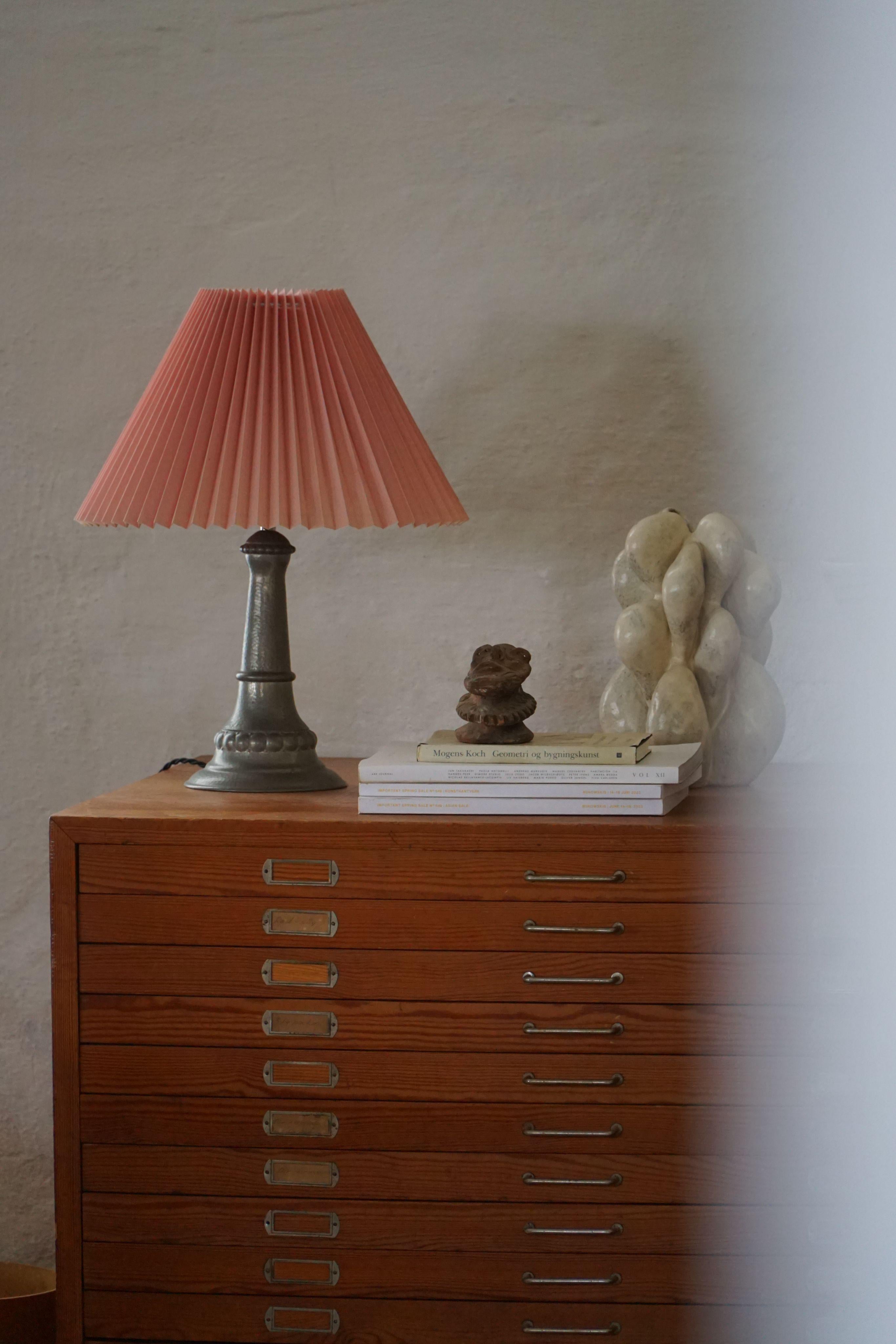 A playful yet elegant table lamp in tin, topped with a soft pink pleated lampshade that spreads a warm, cozy glow. The base has a clean, rounded shape with a slight patina that adds charm and character. It’s simple, but full of personality.
Made in