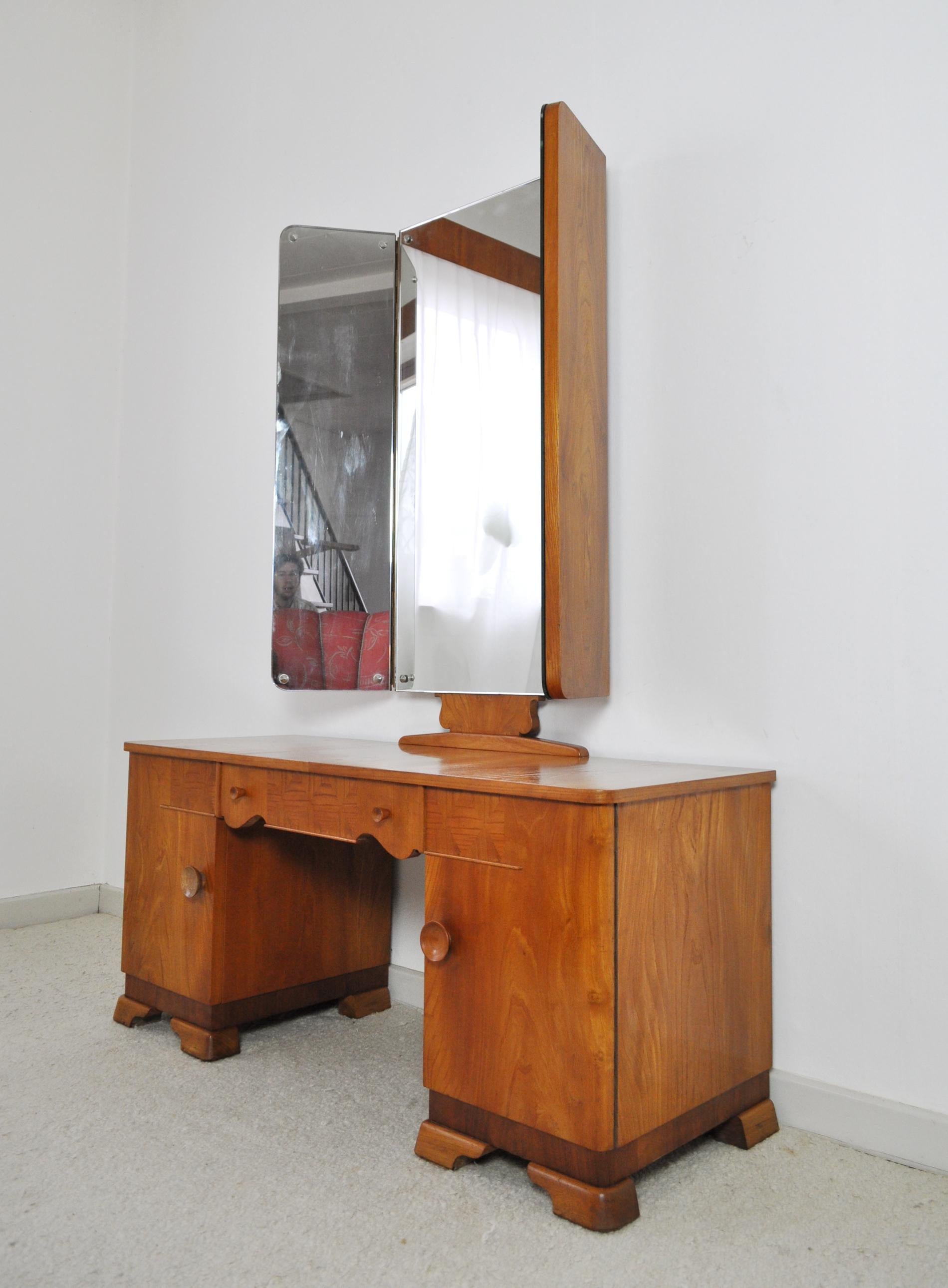 A Danish Art Deco vanity desk with tri-folding mirrors and two small cabinets. Made of mirror cut golden elm veneer.

Fine vintage condition with signs of wear consistent with age and use.
Gently refurbished and top varnished.