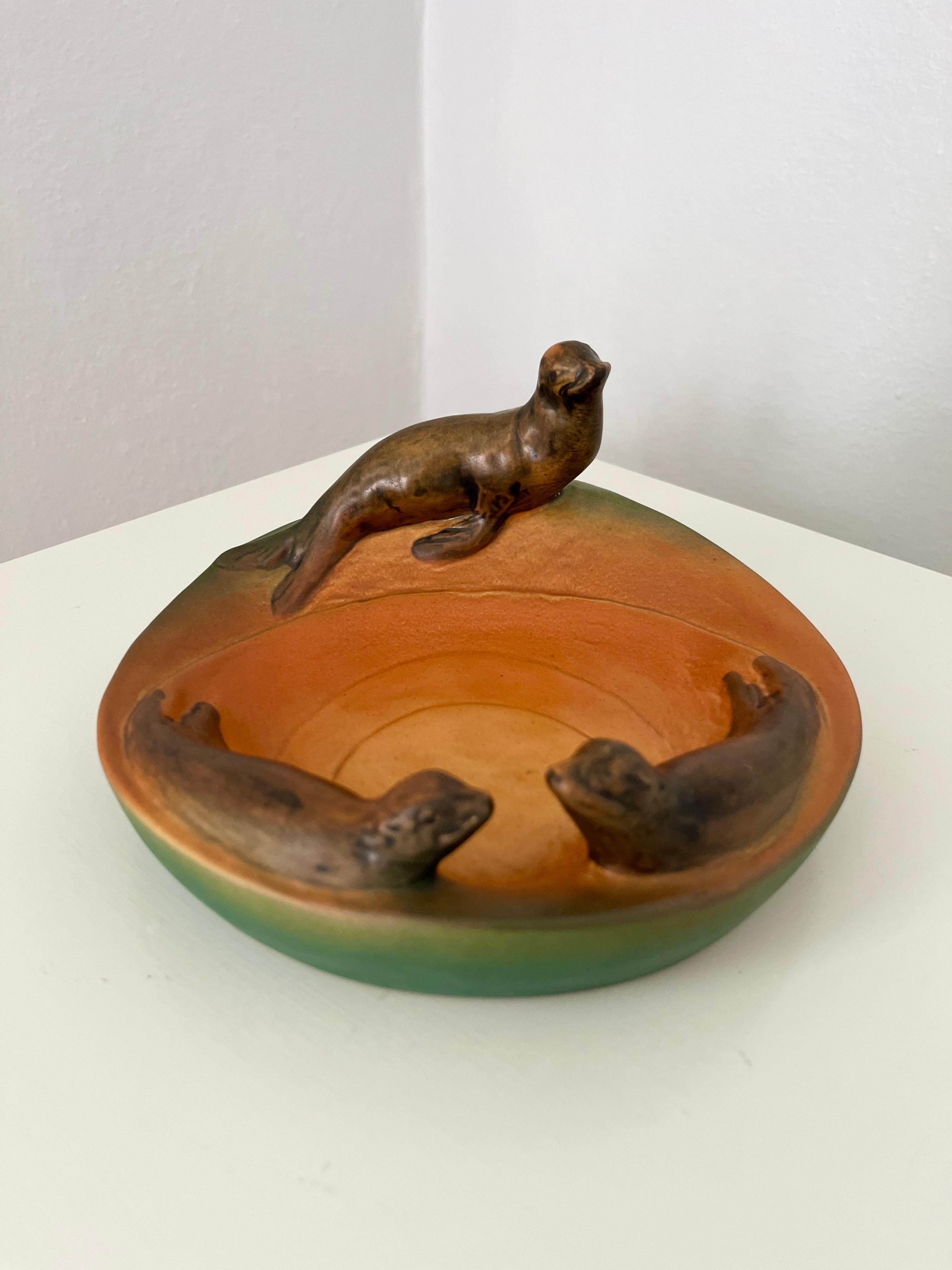 Ciotola danese in stile Art Nouveau con leoni marini di P. Ipsens Enke, 1910/1920

Questa ciotola decorativa in stile Art Nouveau presenta le affascinanti figure di tre leoni marini, con le iconiche tonalità sfumate di verde, arancione e marrone