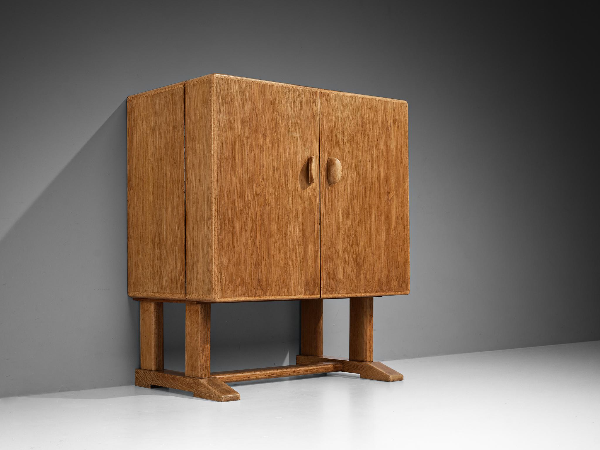 Mobile bar, Oak, vetro, Danimarca, anni '60

Robusto mobile bar danese in legno massiccio di Oak. Il mobile cubico poggia su due gambe accoppiate con un'assicella di collegamento. Due maniglie decorative e intagliate accedono all'interno. Molteplici