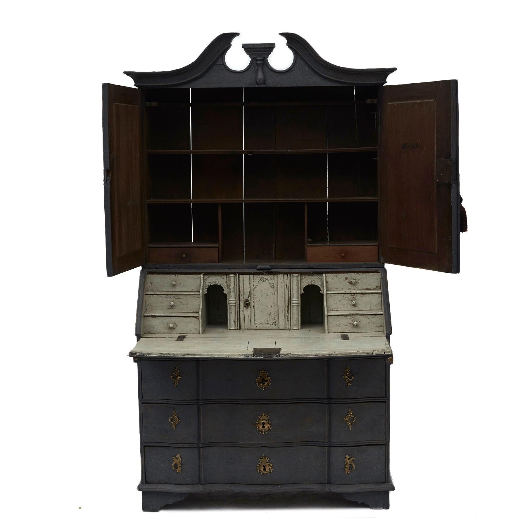 Danish baroque bureau in two parts in oak, painted in dark grey.
Upper cupboard with swan neck top and a pair of baroque doors with fillings. Lower part with four drawers (three large and one smaller) 
Straight split front. 
Above drawers slanted