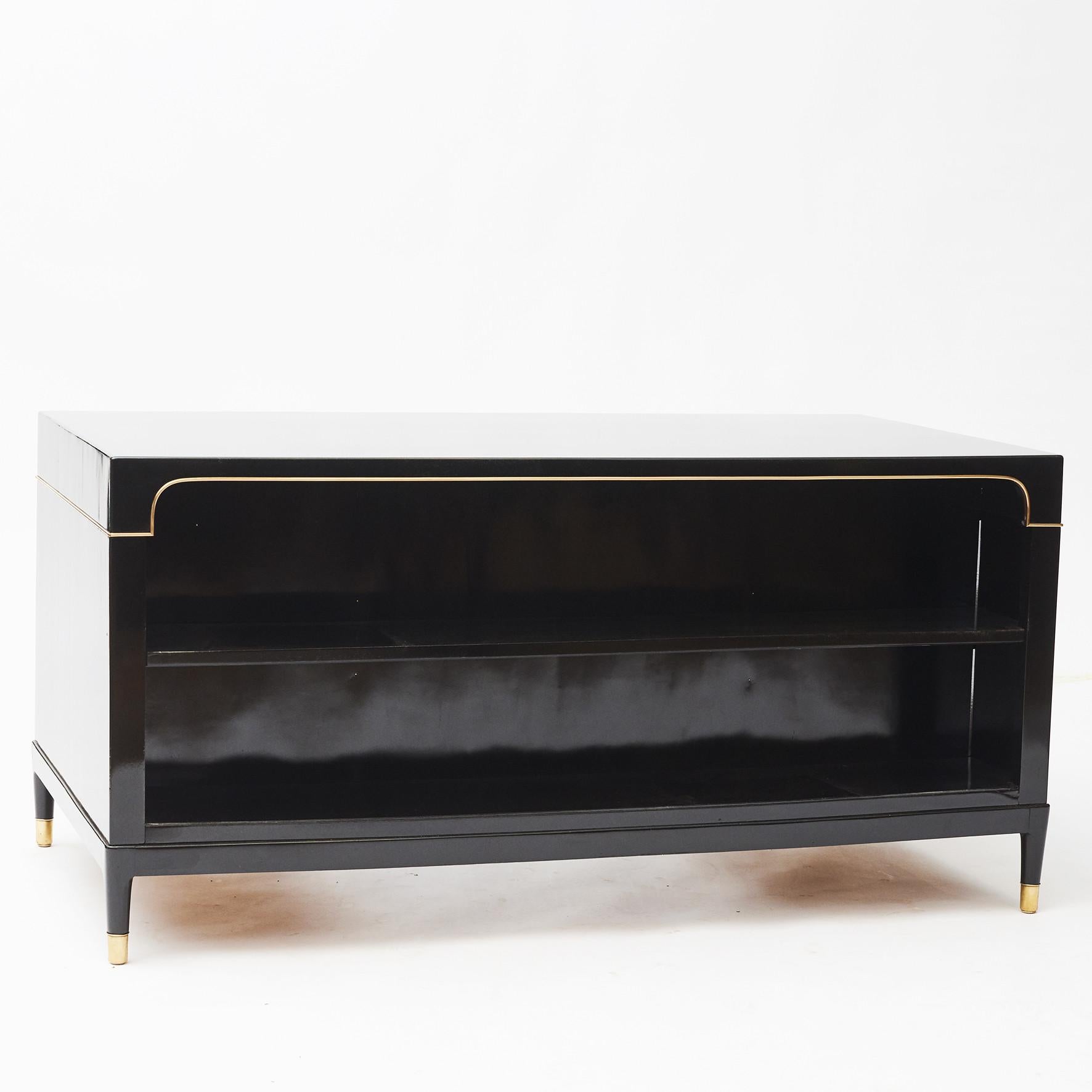 Freestanding desk in high-gloss black lacquered mahogany. The front includes drawers and a door, shelves to the opposite side of the desk.
Freestanding
Adorned with an all around brass trim.
This desk is raised by eight legs with brass foot