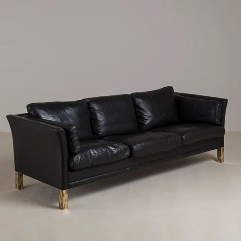 A Danish black leather upholstered three seater sofa, designed by Mogens Hansen, with additional sculpted brutalist style brass legs, 1950s.

Additional Information:
Dimensions: 77 H x 217 W x 72 H cm.