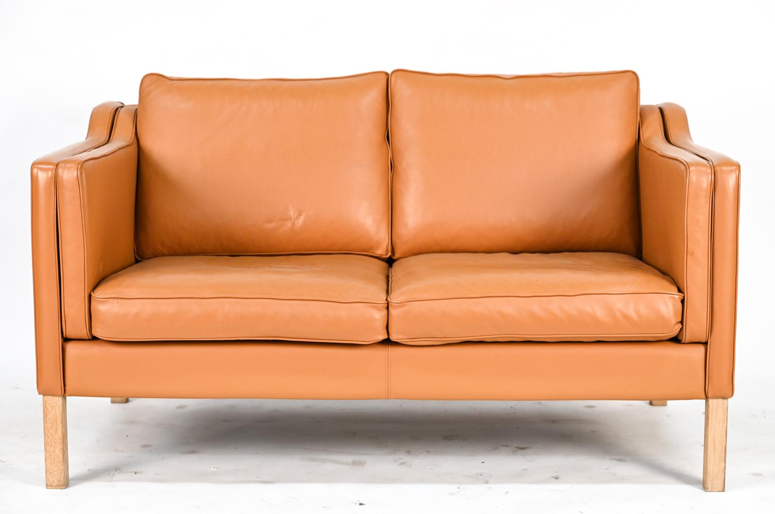 A Danish mid-century sofa suite comprised of a three-seater sofa and two-seater loveseat upholstered in handsomely patinated brandy leather. In the manner of iconic Scandinavian designer Borge Mogensen.