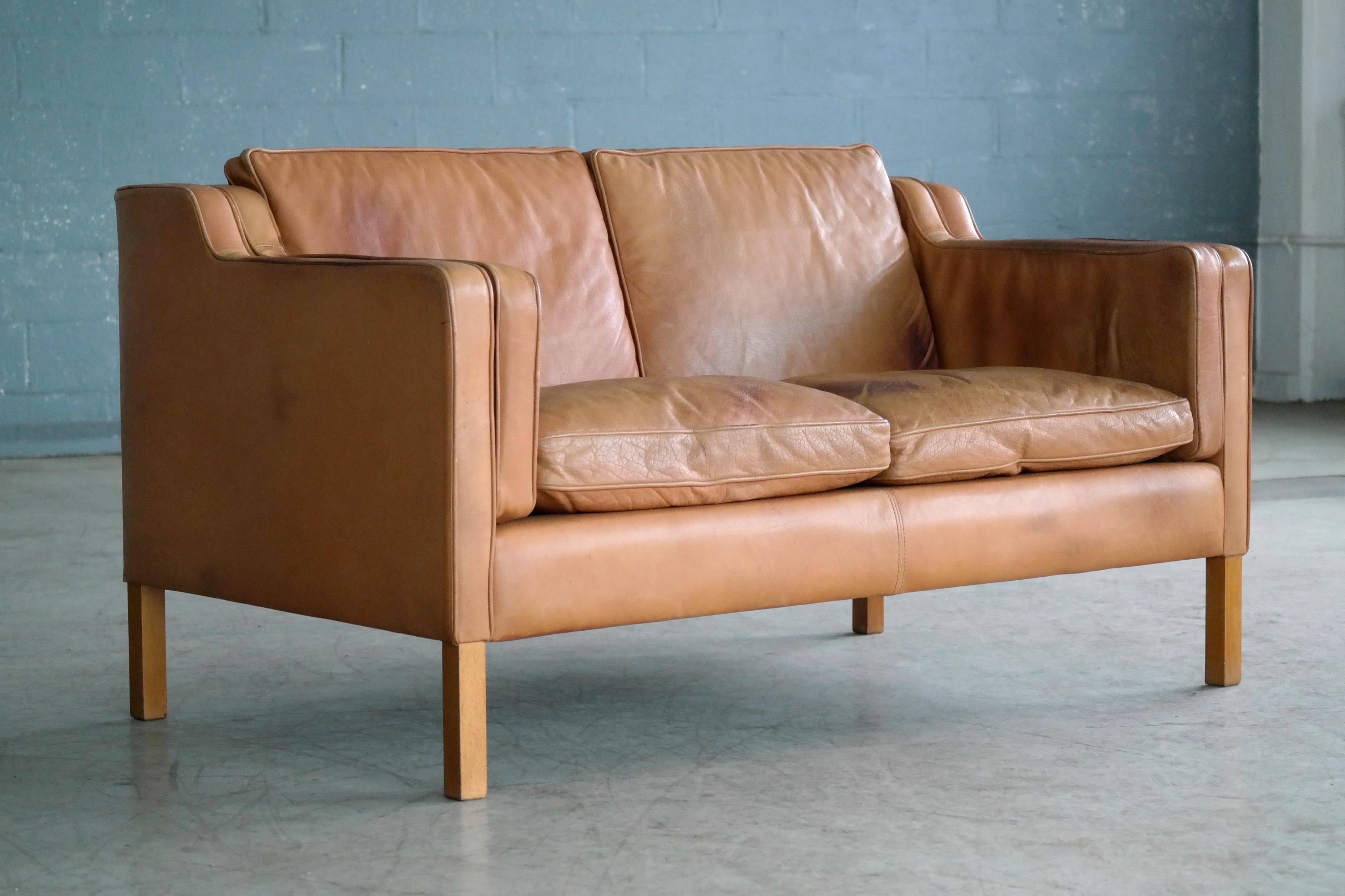 Classic Danish two-seat sofa in the style of Borge Mogensen's model 2212. Executed in supple tan leather by Stouby Mobler raised on beech legs. Mogensen's Classic design has become a staple of modern decor as his sofas set a new standard for
