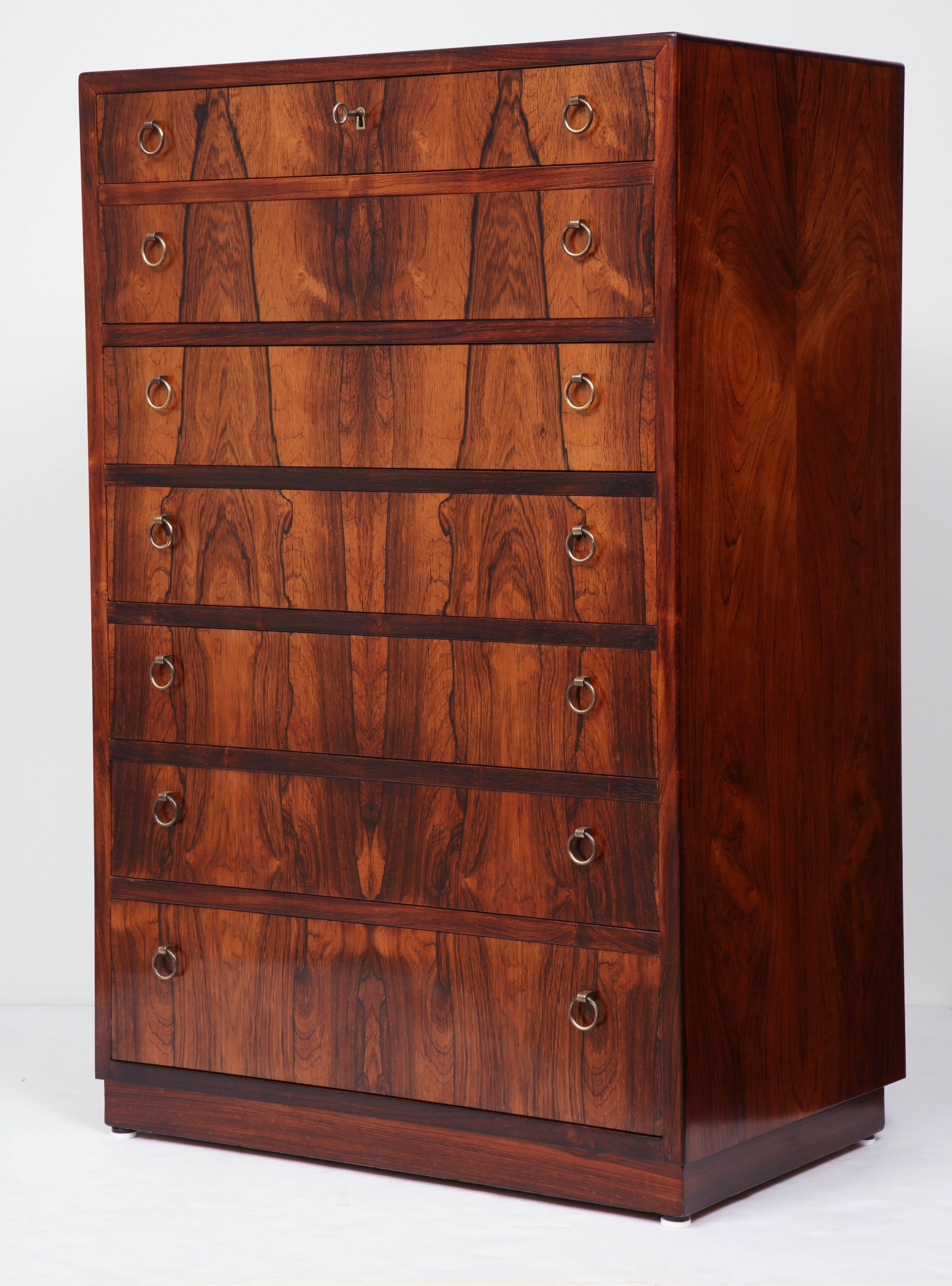 A Danish Brazilian rosewood tall chest of drawers, circa 1940s, of rectangular form with seven graduated drawers and brass ring pulls, raised on a plinth base. Beautiful and striking rosewood veneer on all sides.