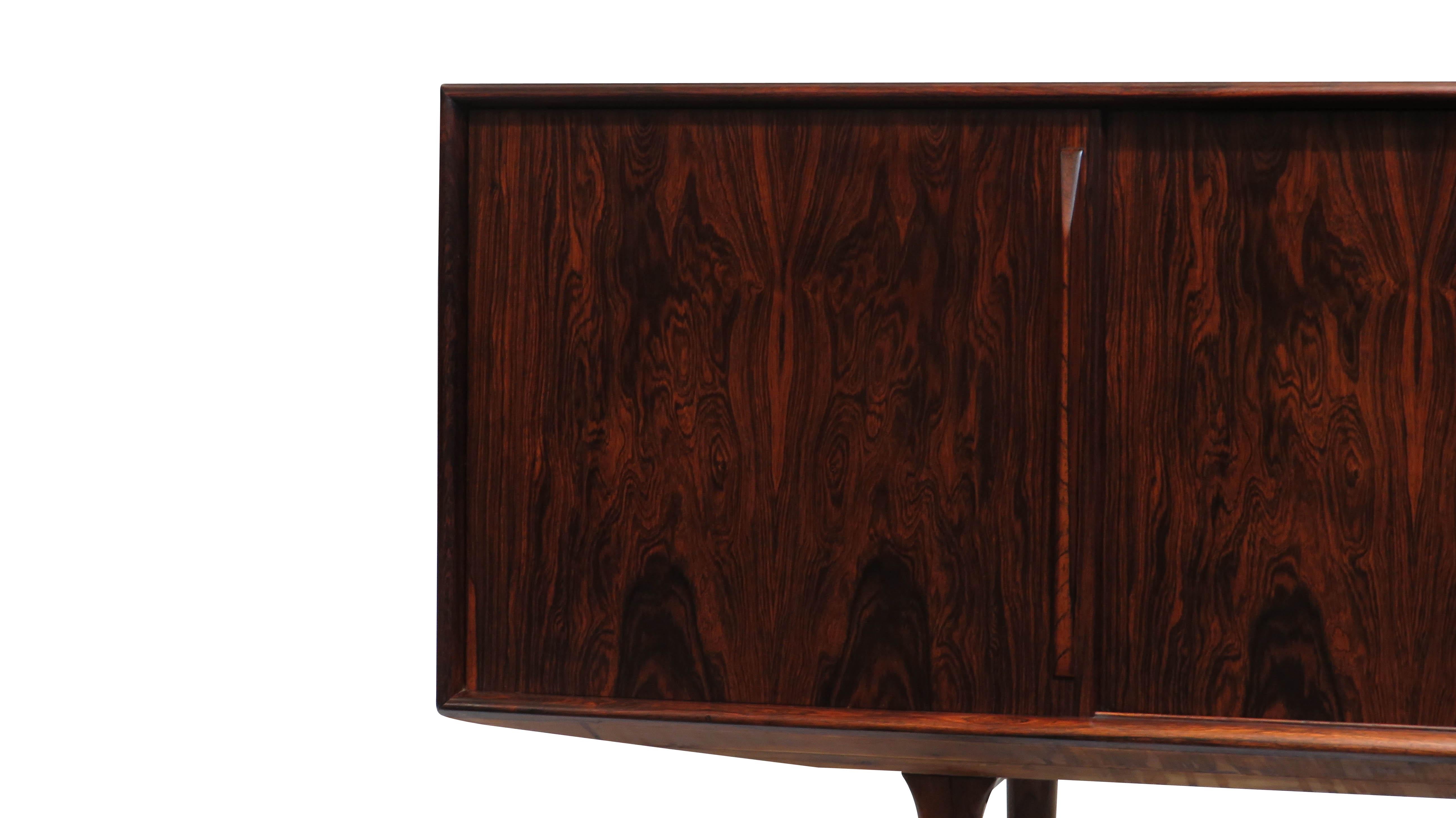 Danish credenza handcrafted of dark Brazilian rosewood with stunning book-matched grain on four sliding doors. Beech wood interior with adjustable shelves. Raised on tapered legs. The cabinet is fully restored in a natural oil finish, and in
