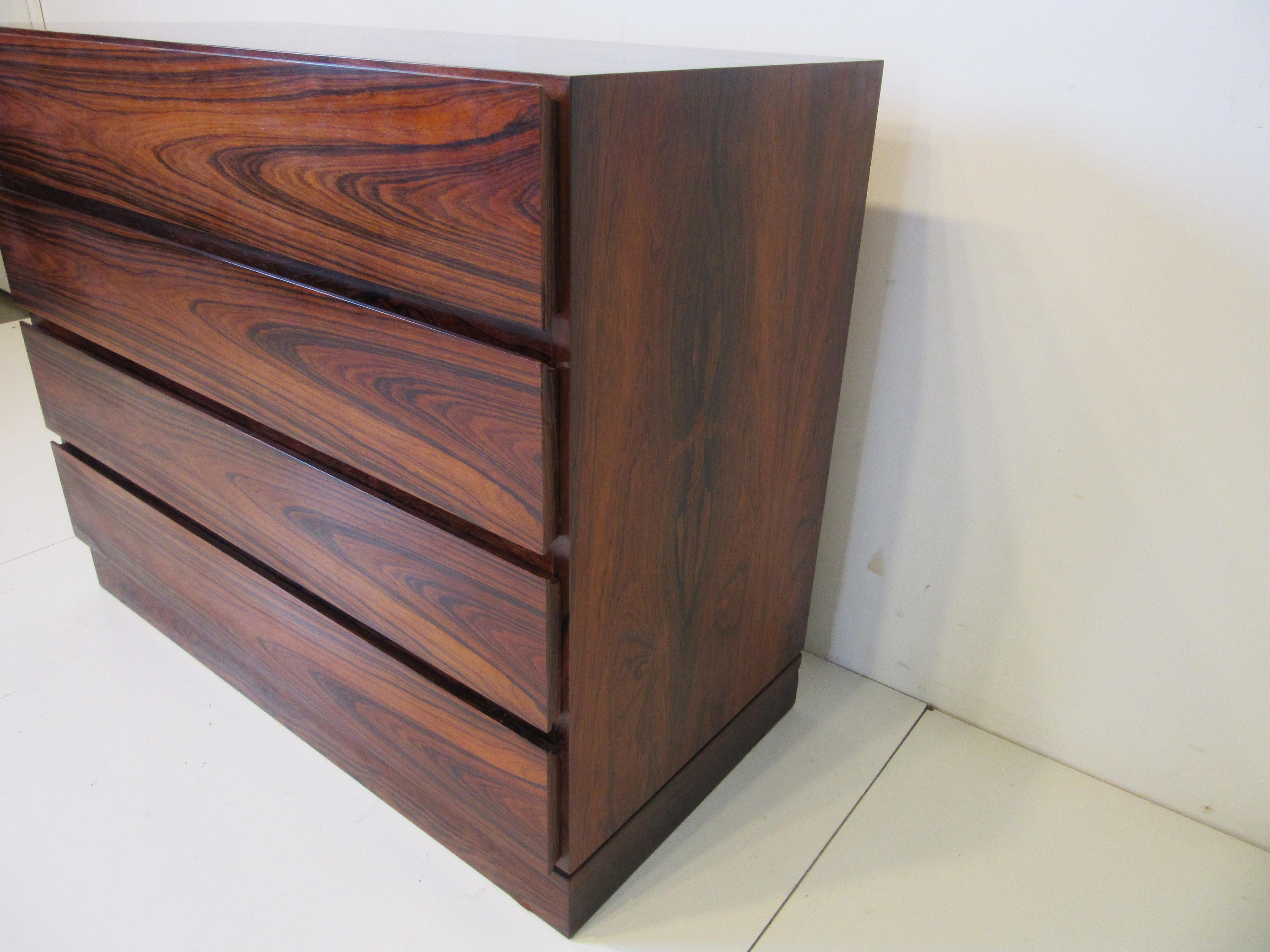A rich well grained Brazilian rosewood four drawer dresser with the lower part of the drawer fronts curved for finger pulls . manufactured and ink stamped to the bottom of the base Made In Denmark, a great eye catching design that is well crafted.