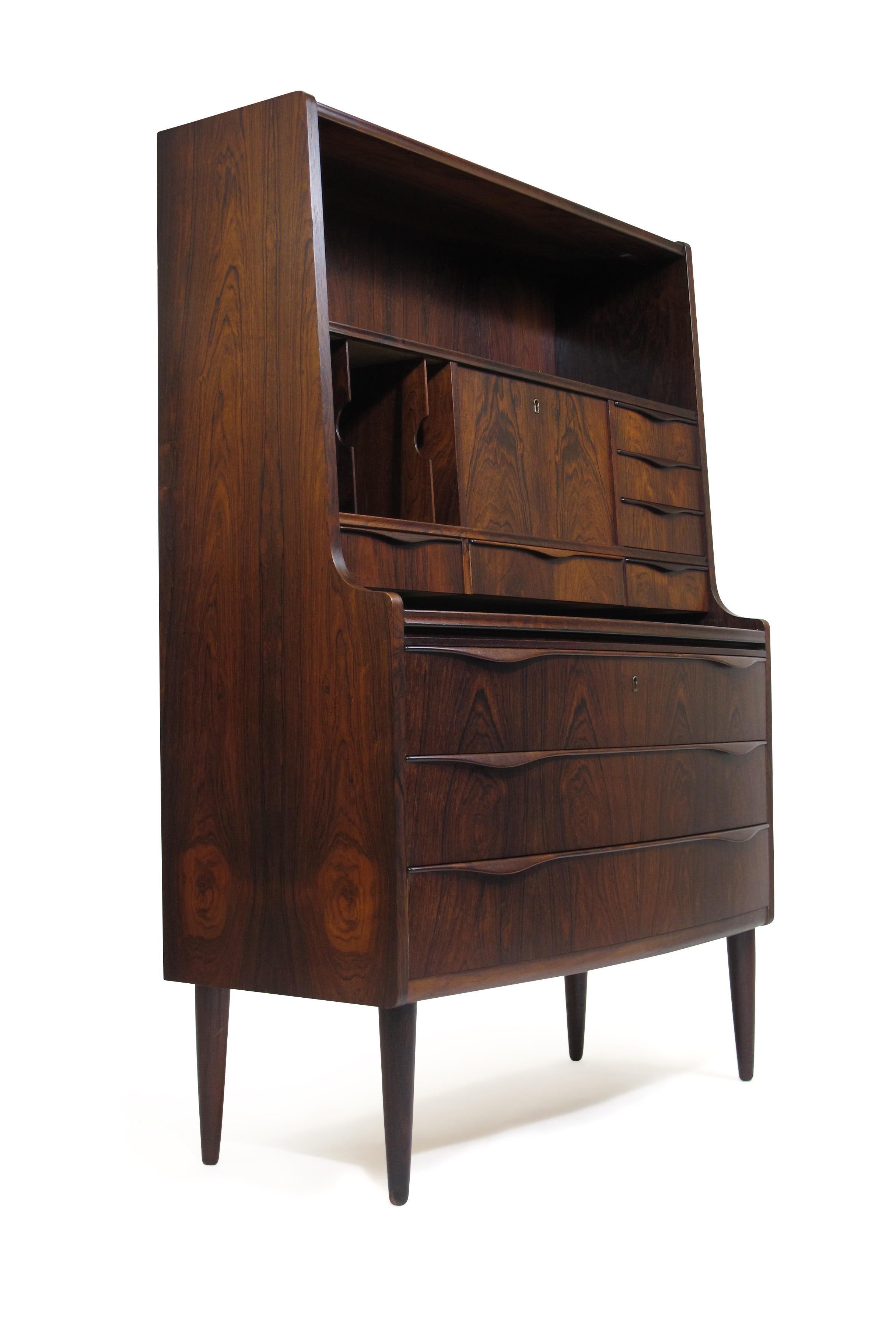 Rosewood Danish secretary desk attributed to Kofod-Larsen, manufactured in Denmark. Dark book-matched rosewood grain with extensive storage including: 3 large drawers, multiple small drawers, locked compartment, document drivers and pull out desk.