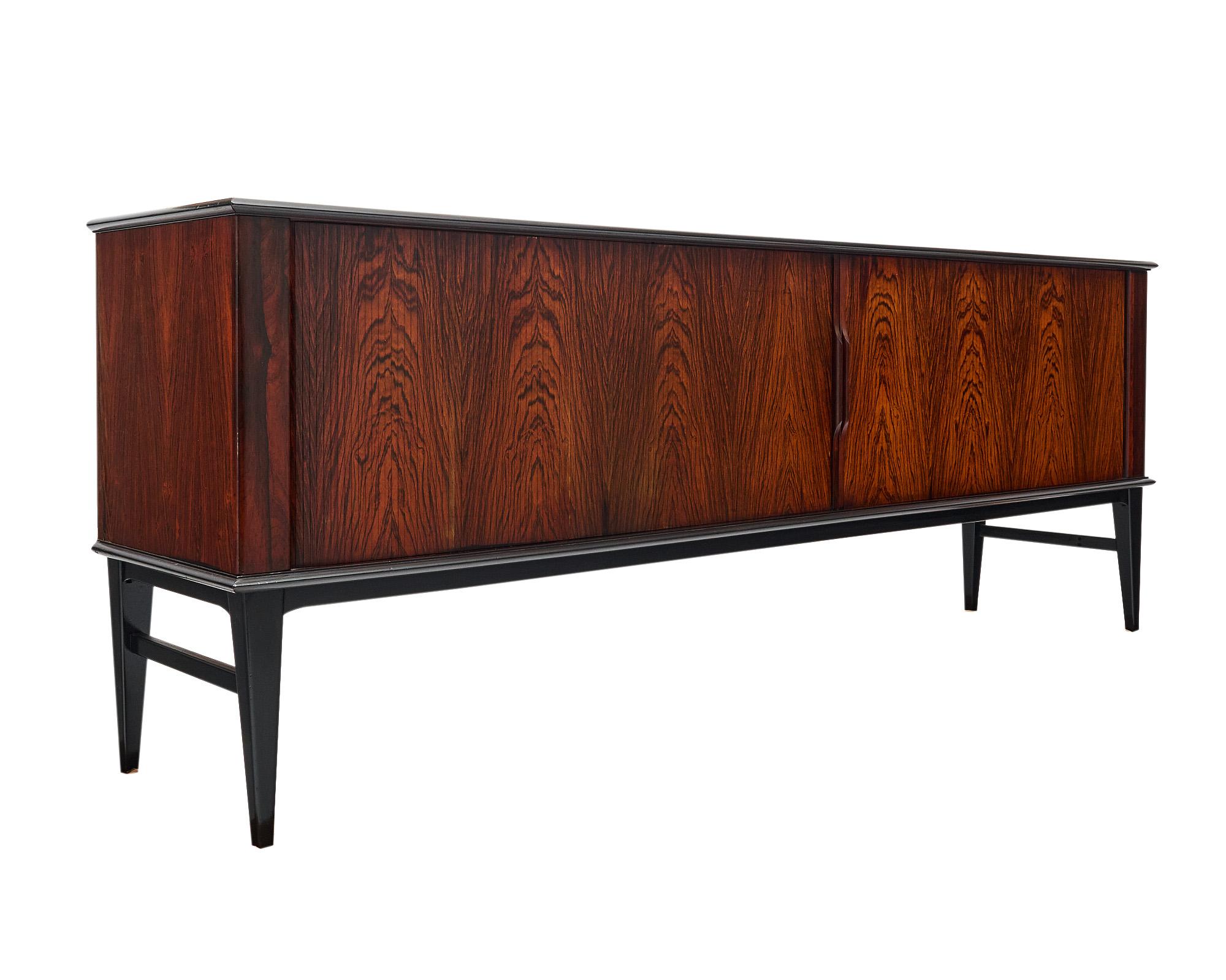 Enfilade or buffet, Danish, made of striking Brazilian Rosewood. The sideboard features tapered legs and “tambour doors“ with hand-carved wood handles opening to interior shelving and four central dovetailed drawers. The drawers are felt lined. This