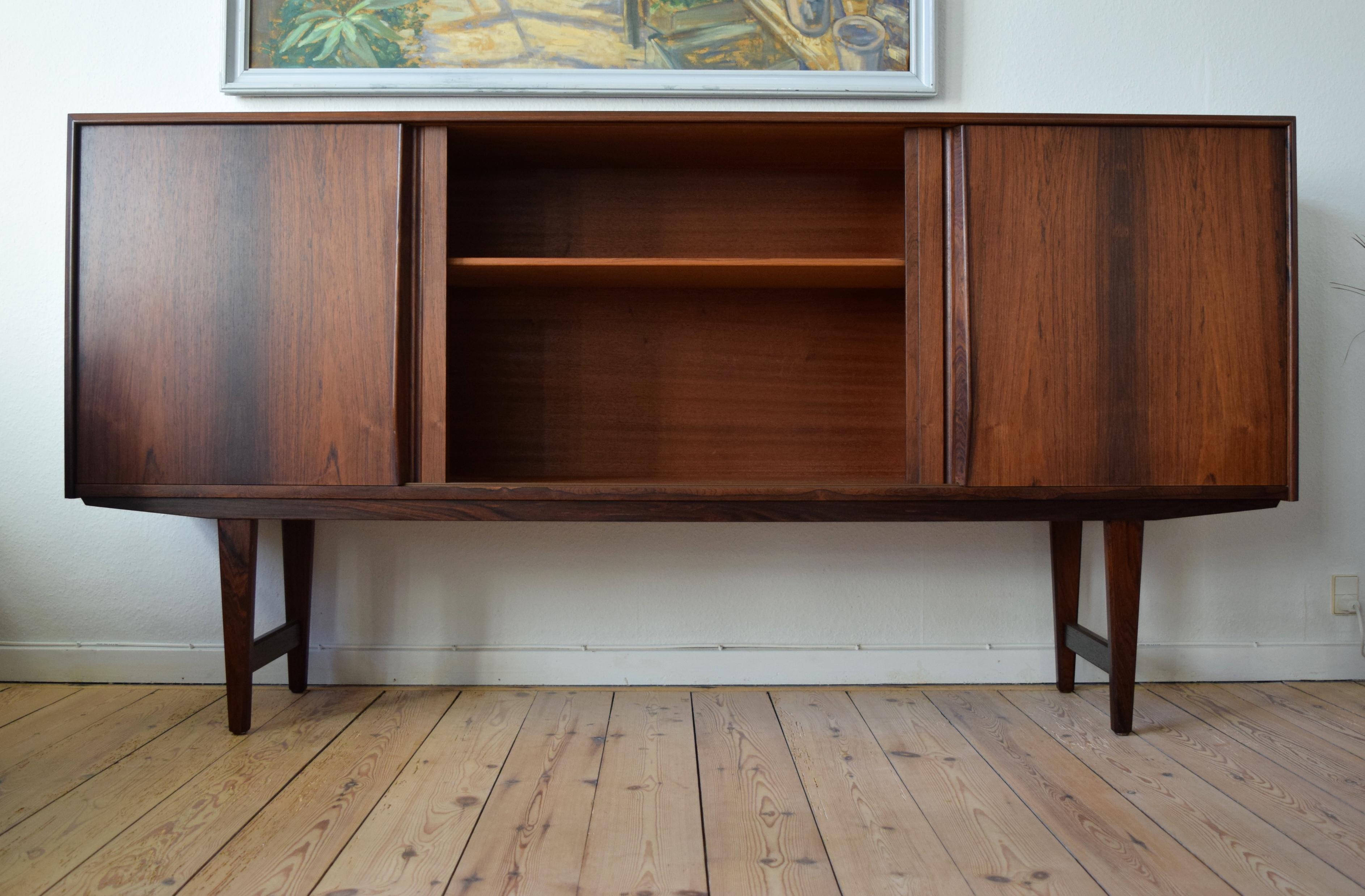 Brazilian rosewood low sideboard designed by E.W. Bach manufactured by Sejling Skabe in Denmark in the 1960s. Four smooth sliding doors on the front with three internal compartments with shelves. The right compartment has a bar section with mirror